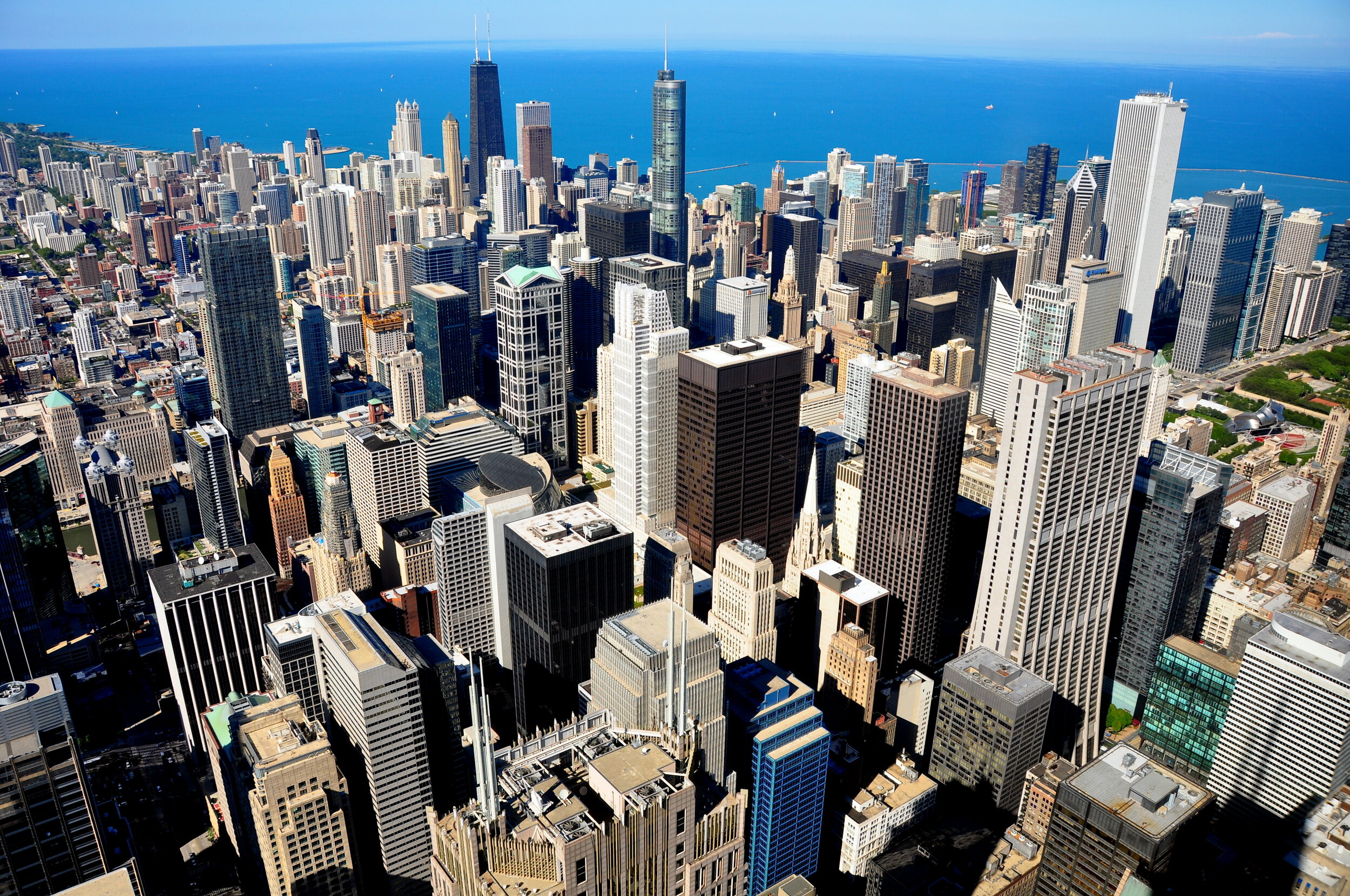 Aerial view of downtown Chicago with numerous skyscrapers, Lake Michigan in the background, and clear blue sky.