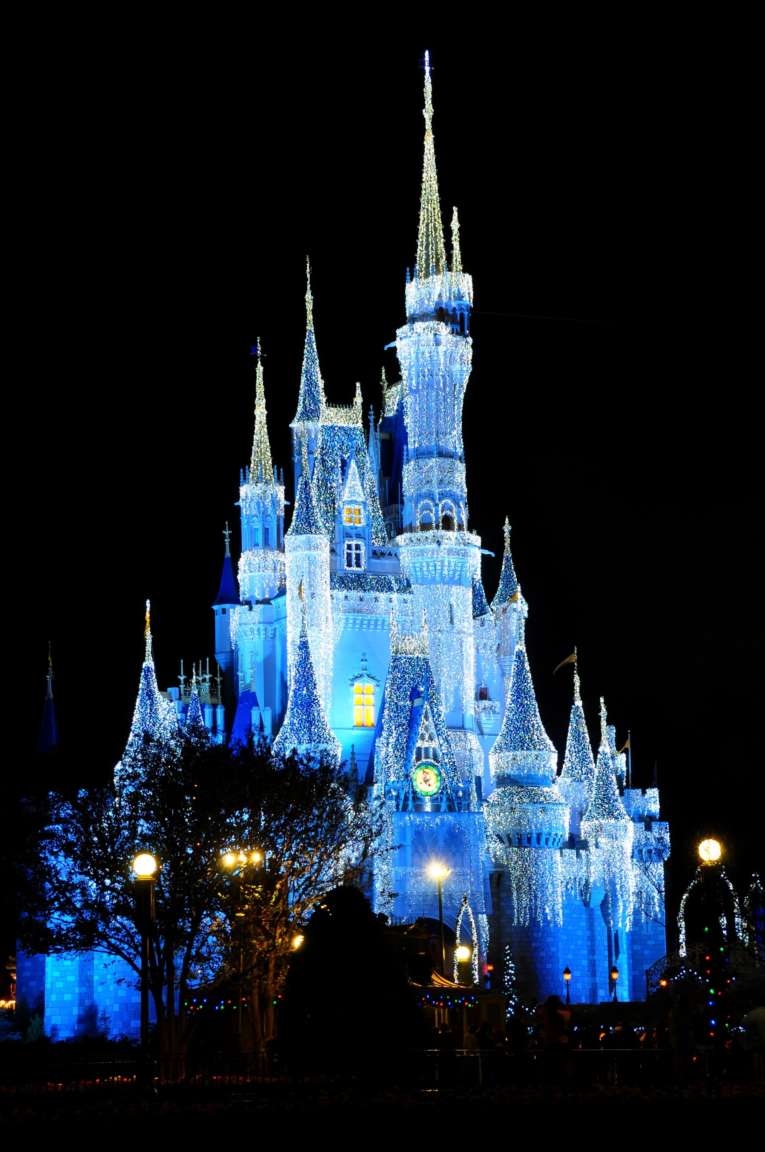 Disney's Cinderella Castle decorated with white and blue Christmas lights at night.