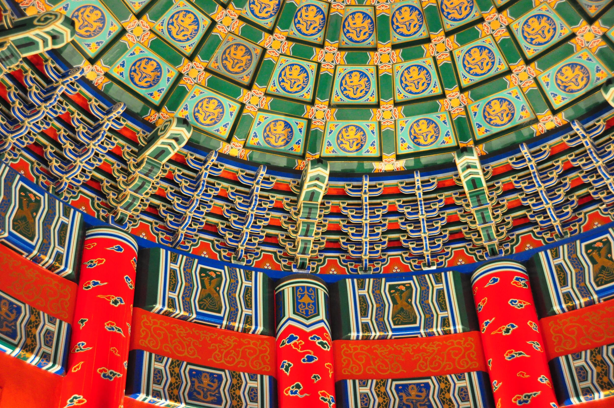 Colorful traditional Asian temple ceiling with intricate patterns, gold accents, and red columns.