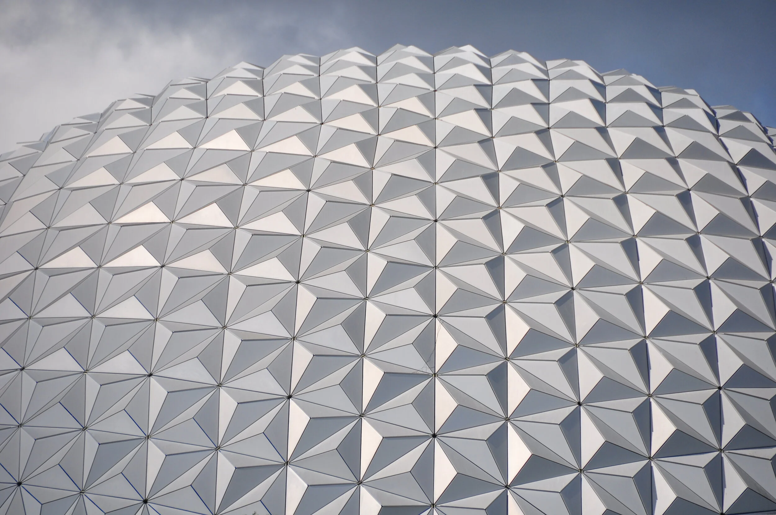 The spaceship Earth geodesic sphere at EPCOT theme park with a pattern of interconnected triangular panels, under a blue sky with a few clouds.