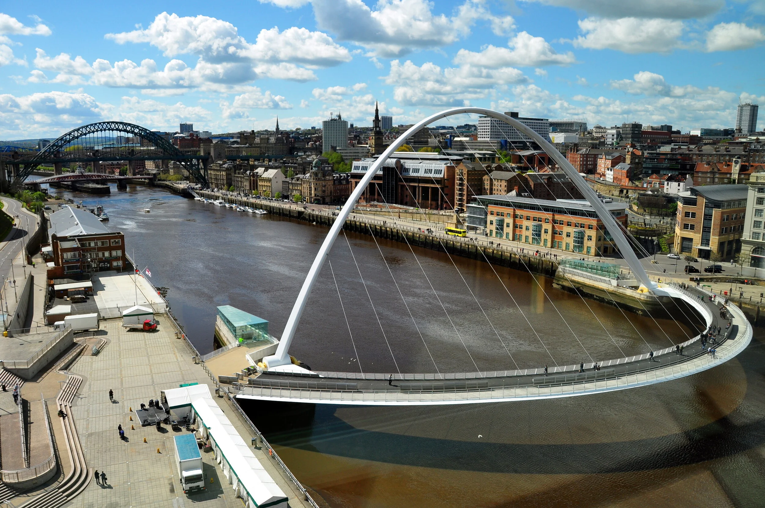 Aerial view of a cityscape with a river, the Millennium Bridge spanning over the river, and other bridges and buildings in the background.