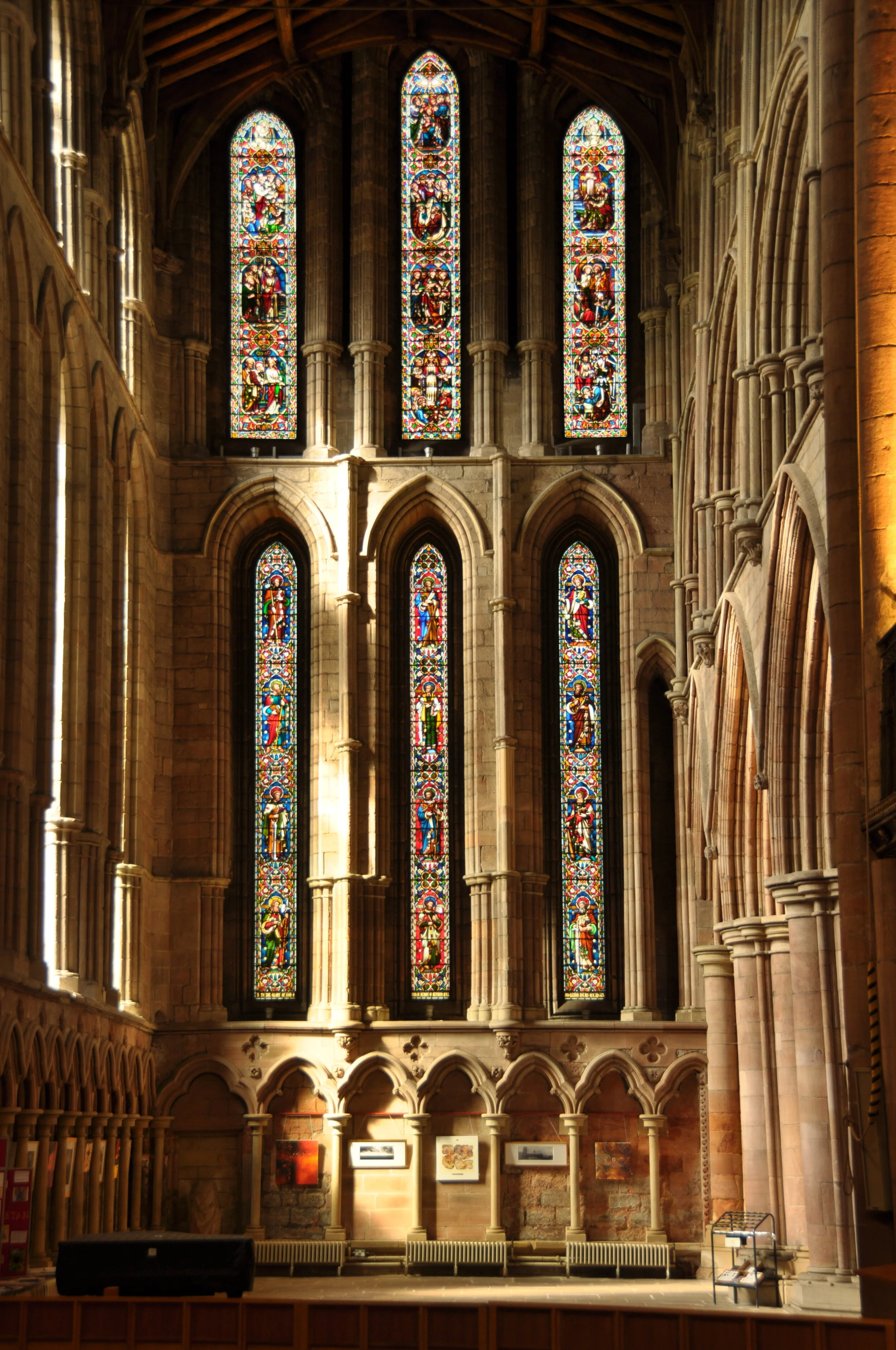 Interior view of a church with stained glass windows, stone columns, and artwork on the walls.