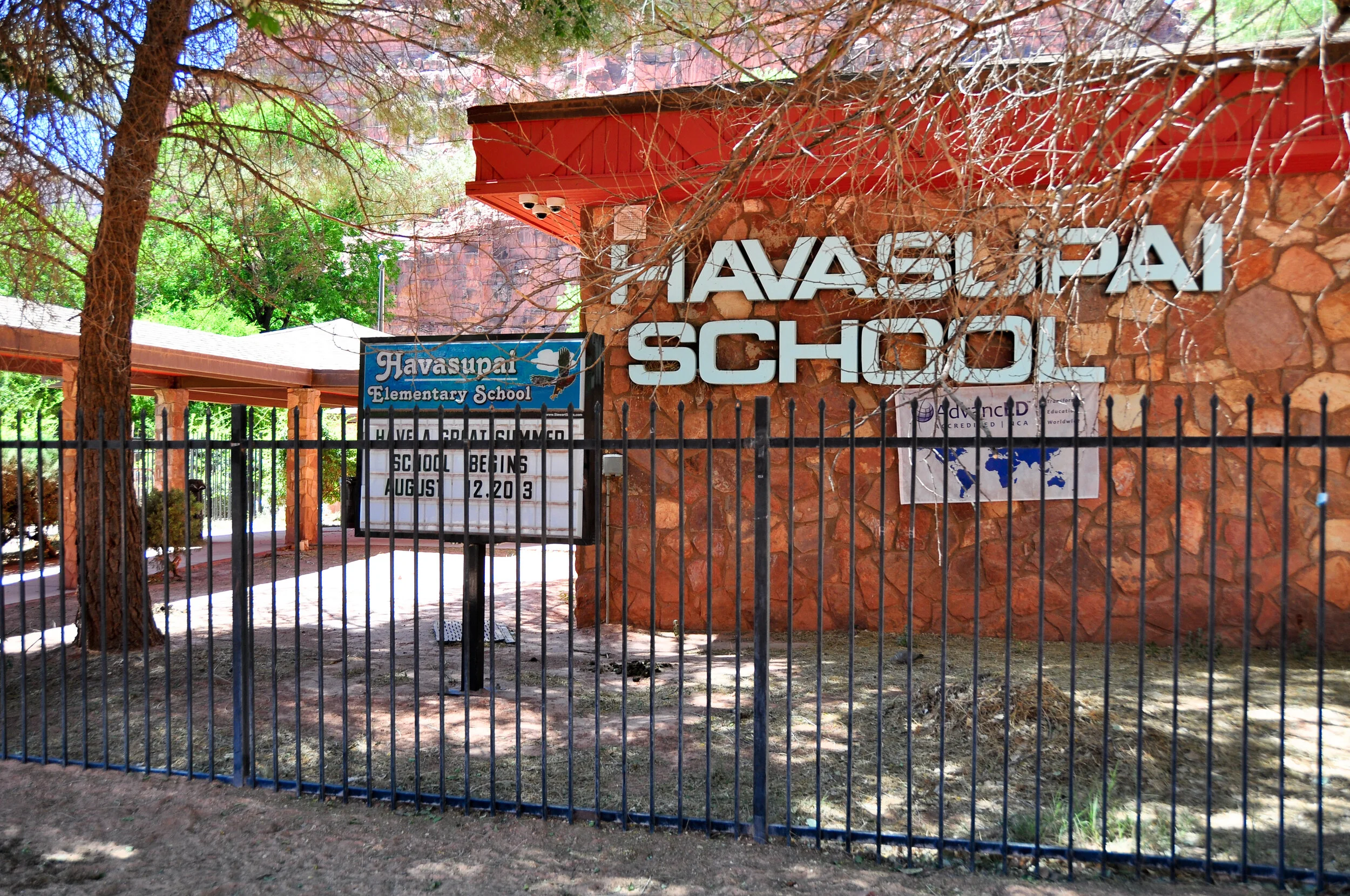 Entrance of Havasupai Elementary School with Metal Sign and Gate, Trees and School Buildings in background.