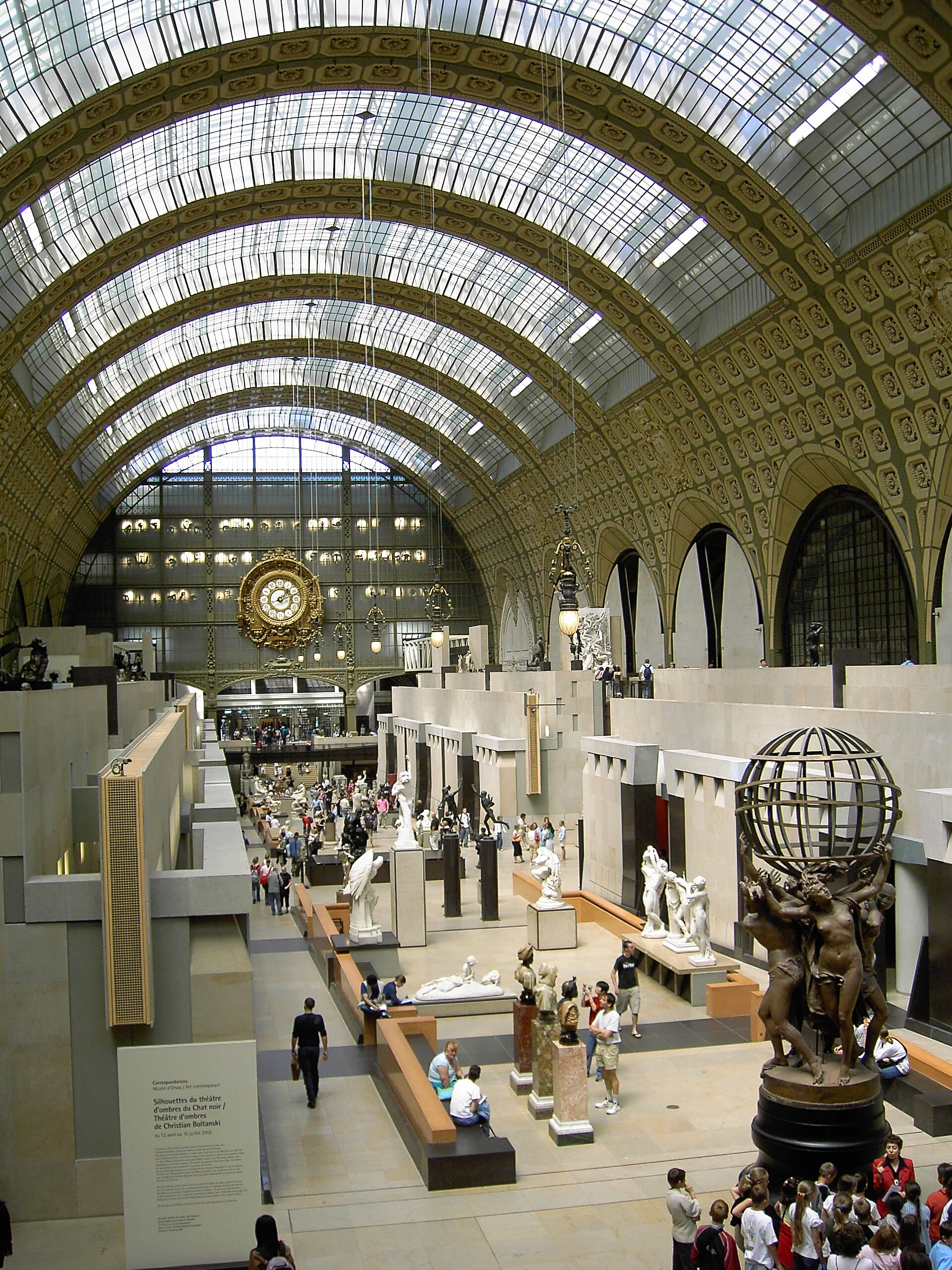 Interior view of the State Hermitage Museum, featuring sculptures and artwork displayed on a spacious, well-lit hall with a high, arched glass ceiling and ornate gold detailing.