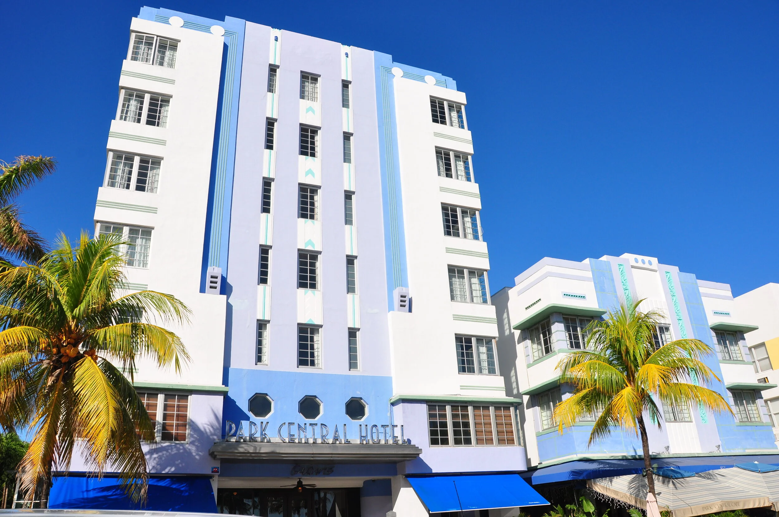 Art Deco style hotel building with palm trees in front, blue sky background, sign reading 'Park Central Hotel' on facade