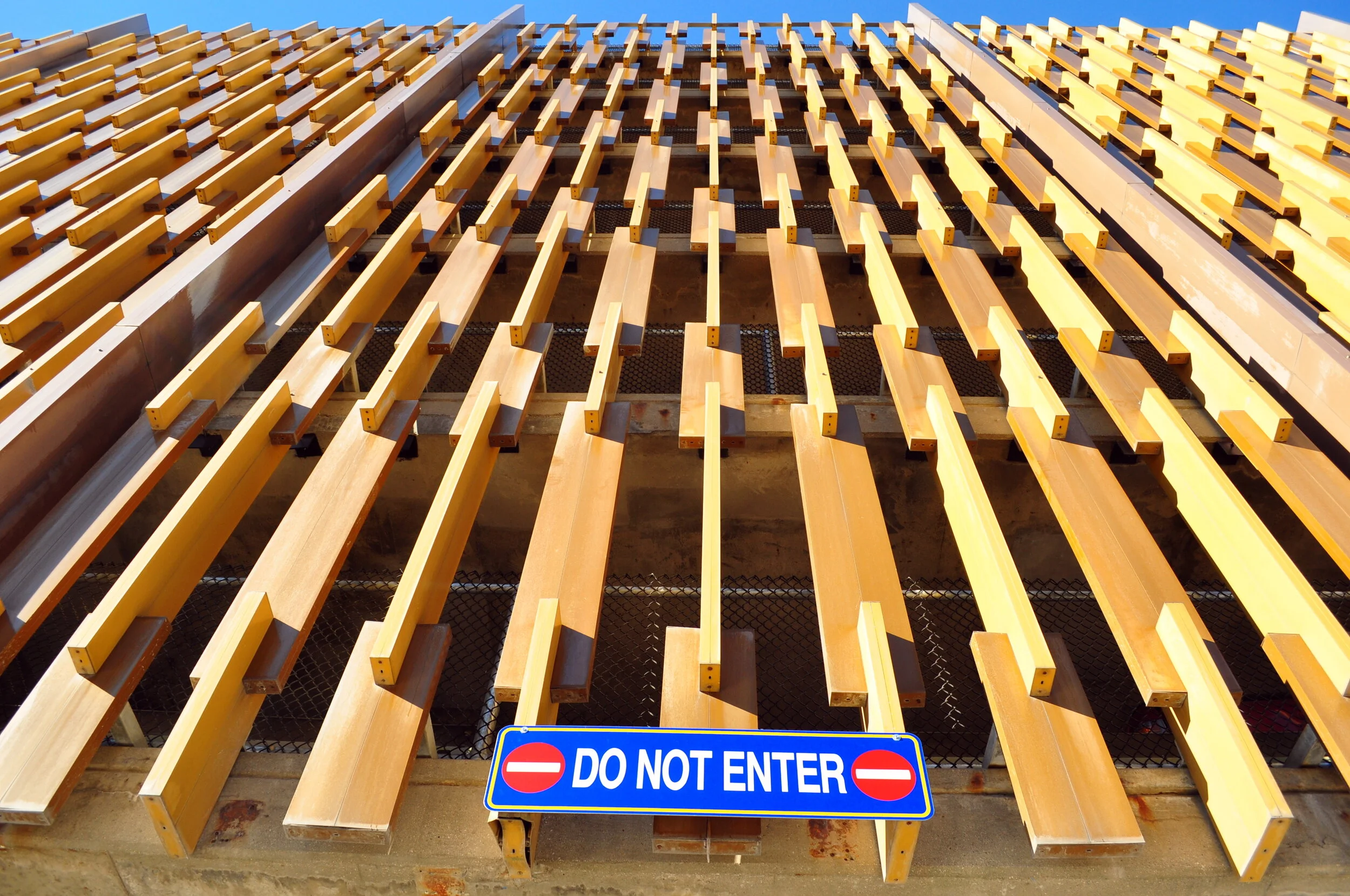 A building facade with wooden louvered panels and a blue and white 'Do Not Enter' sign on a brick wall.