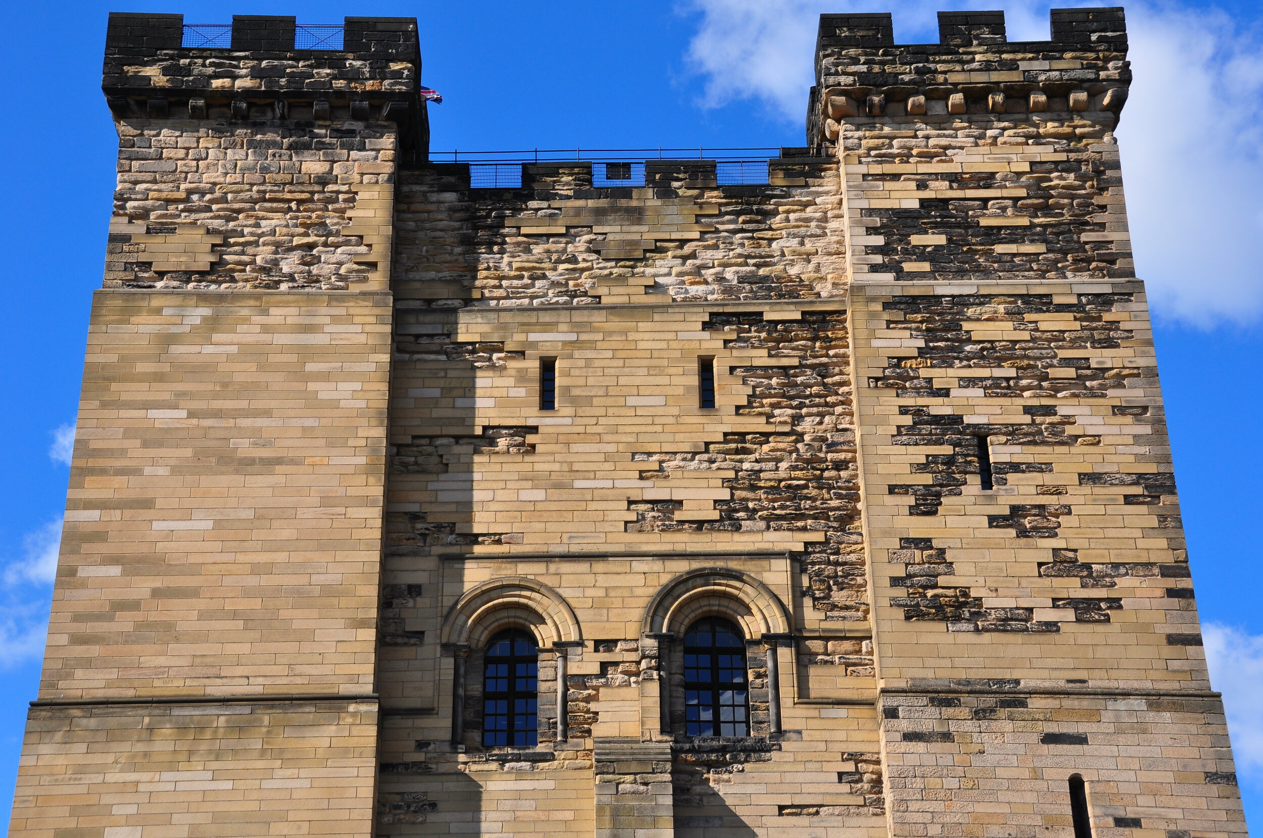 Close-up of an old stone castle tower with narrow windows and battlements against a blue sky.