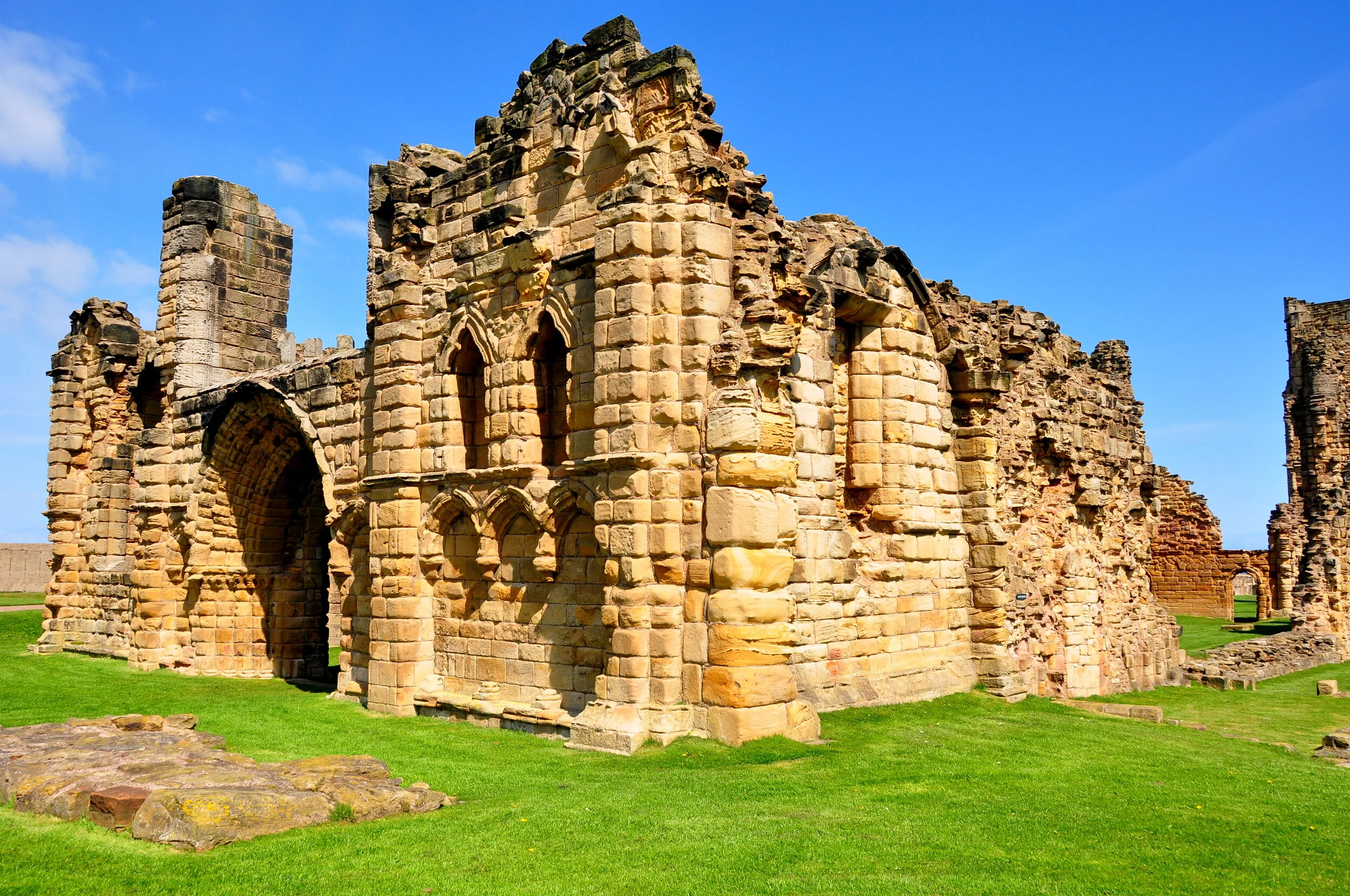 Ruins of an old stone building with arches, set against a bright blue sky and green grass.