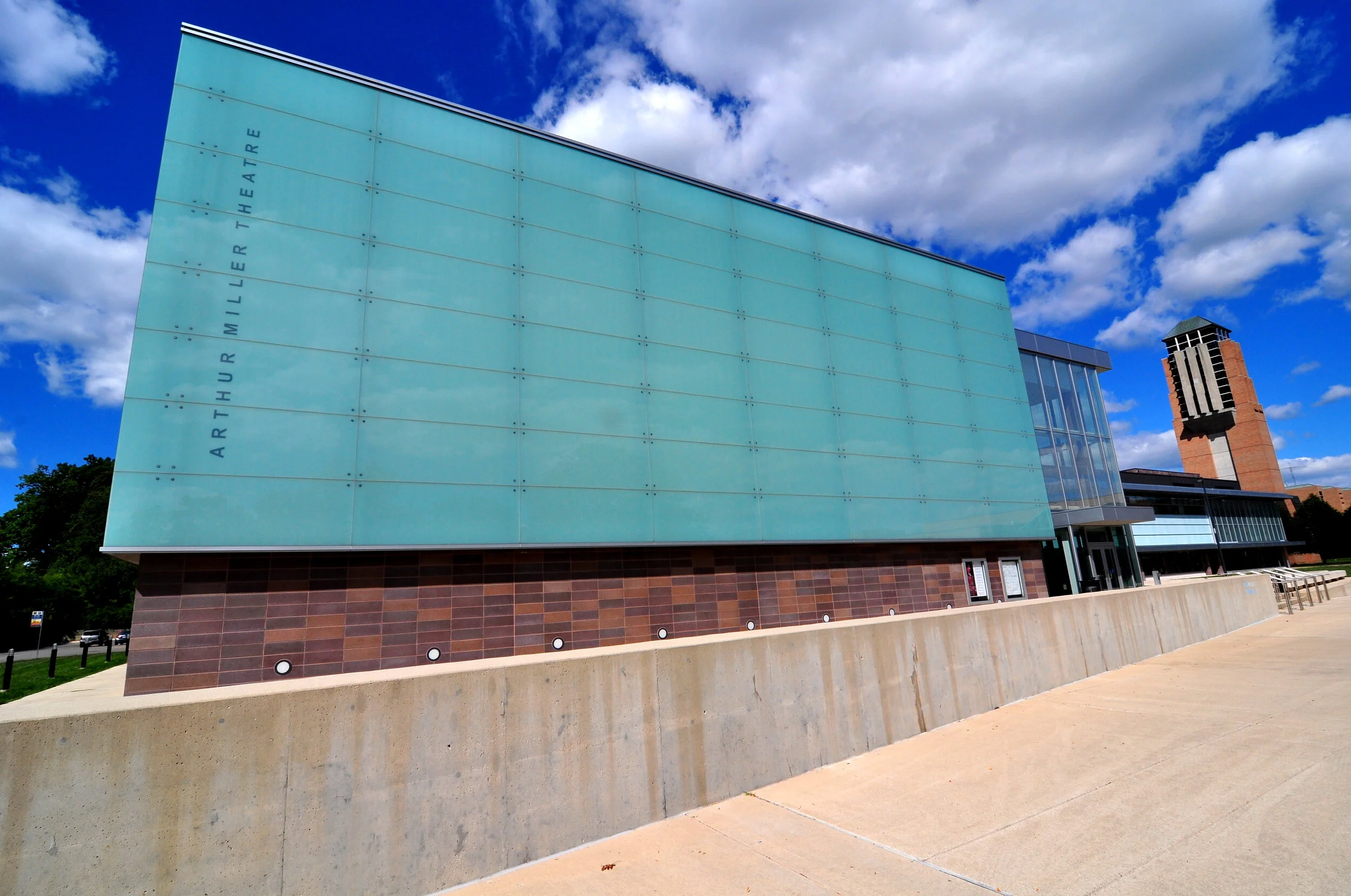 Exterior view of the Arthur Miller Theatre building with a large, light blue facade and clear blue sky with clouds, featuring brick and glass architecture.