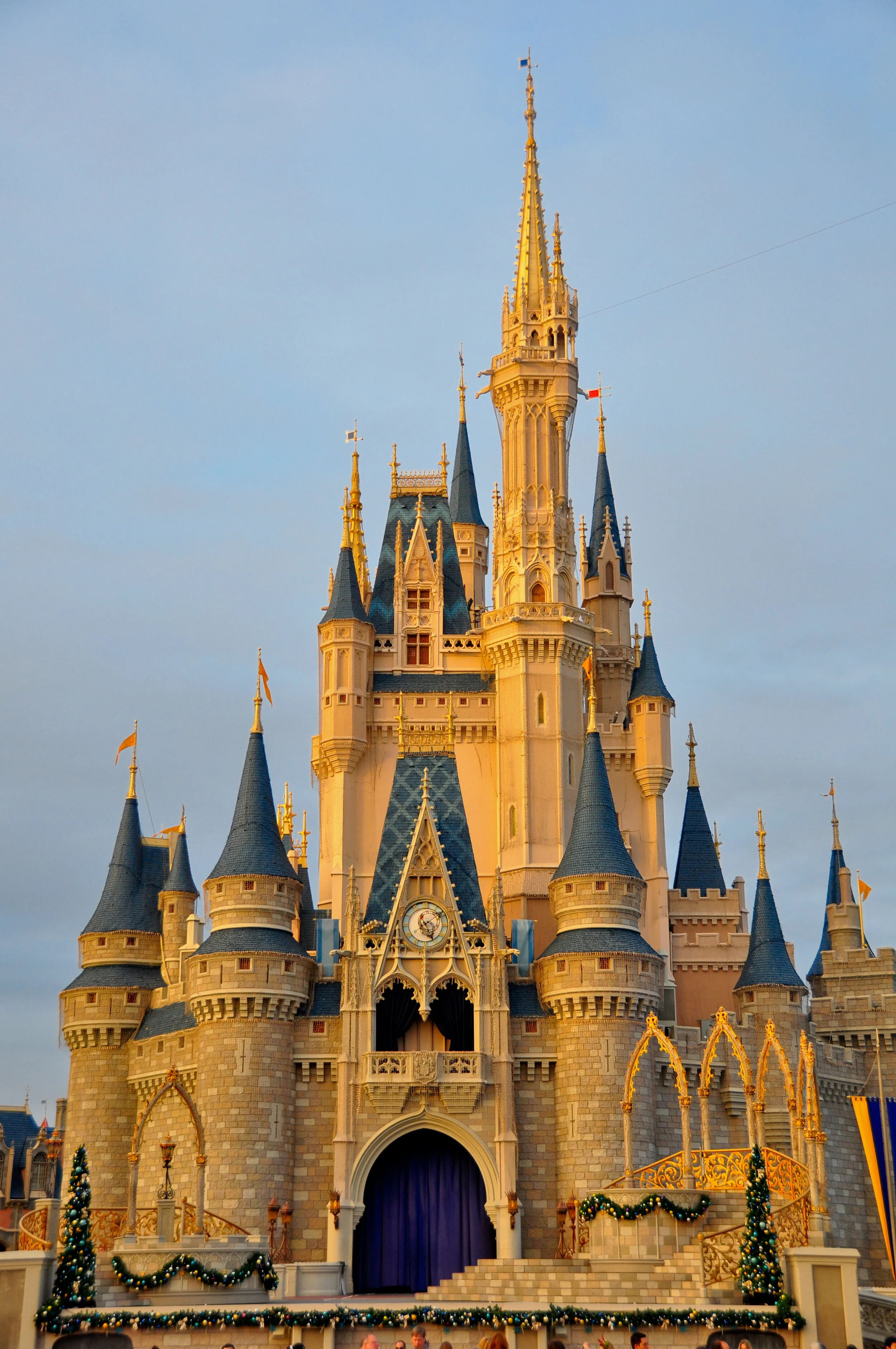 Disney castle decorated with Christmas ornaments and garlands, with a blue curtain at the entrance, set against a partly cloudy sky.