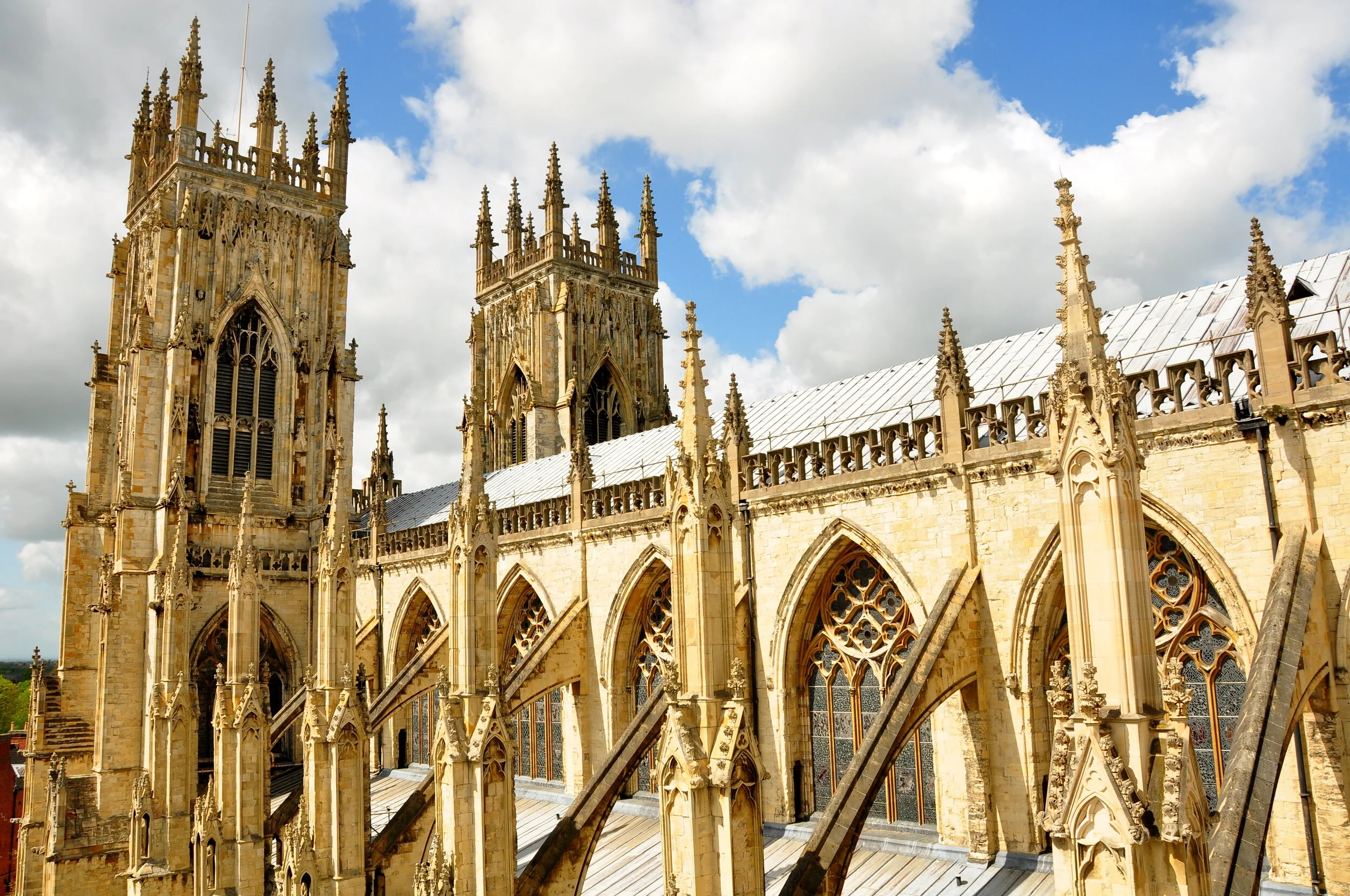 Exterior view of a Gothic cathedral with tall spires, large stained glass windows, and flying buttresses, under a partly cloudy sky.