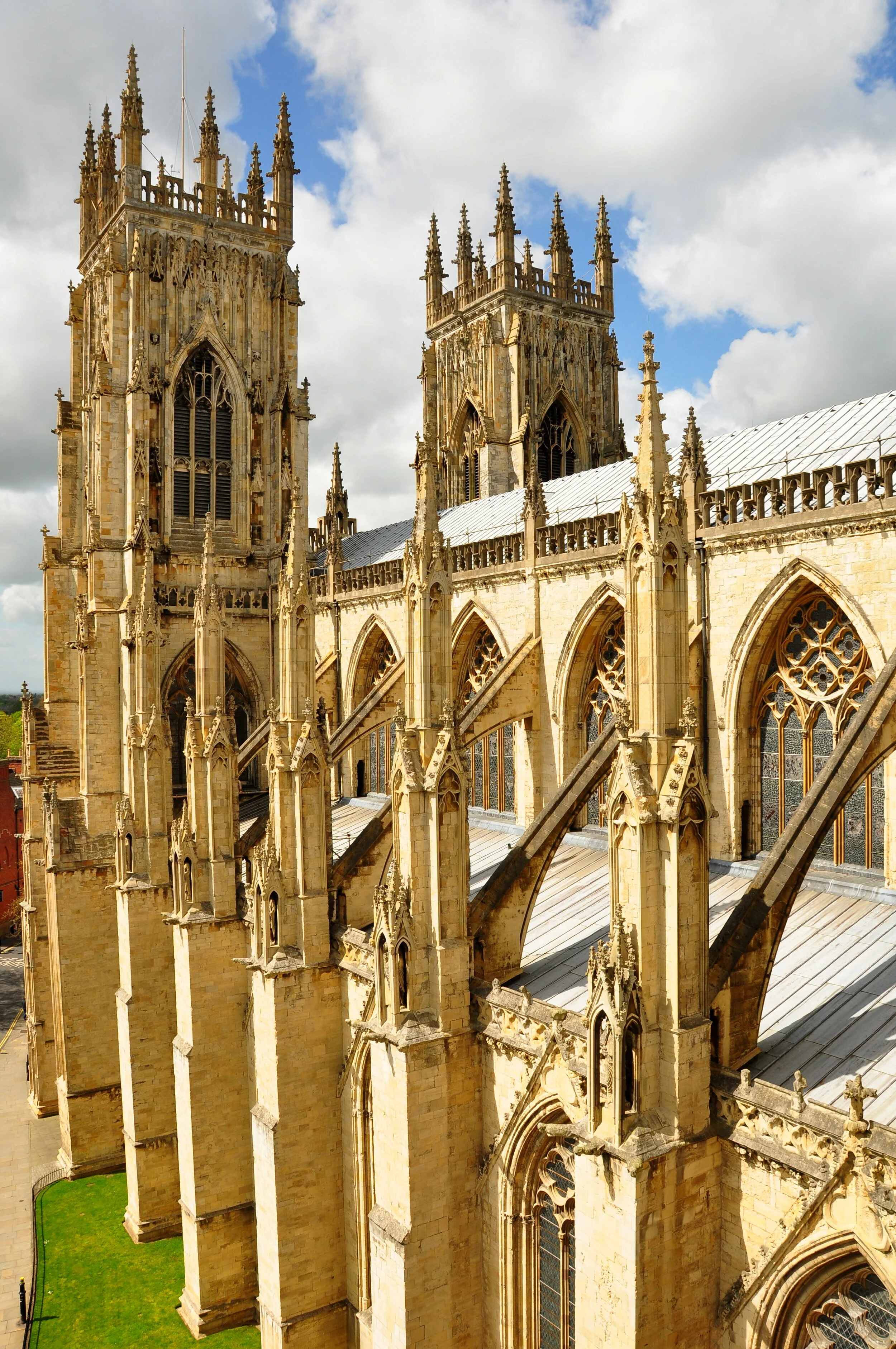 Exterior view of a Gothic cathedral with tall spires, flying buttresses, and detailed stonework against a partly cloudy sky.