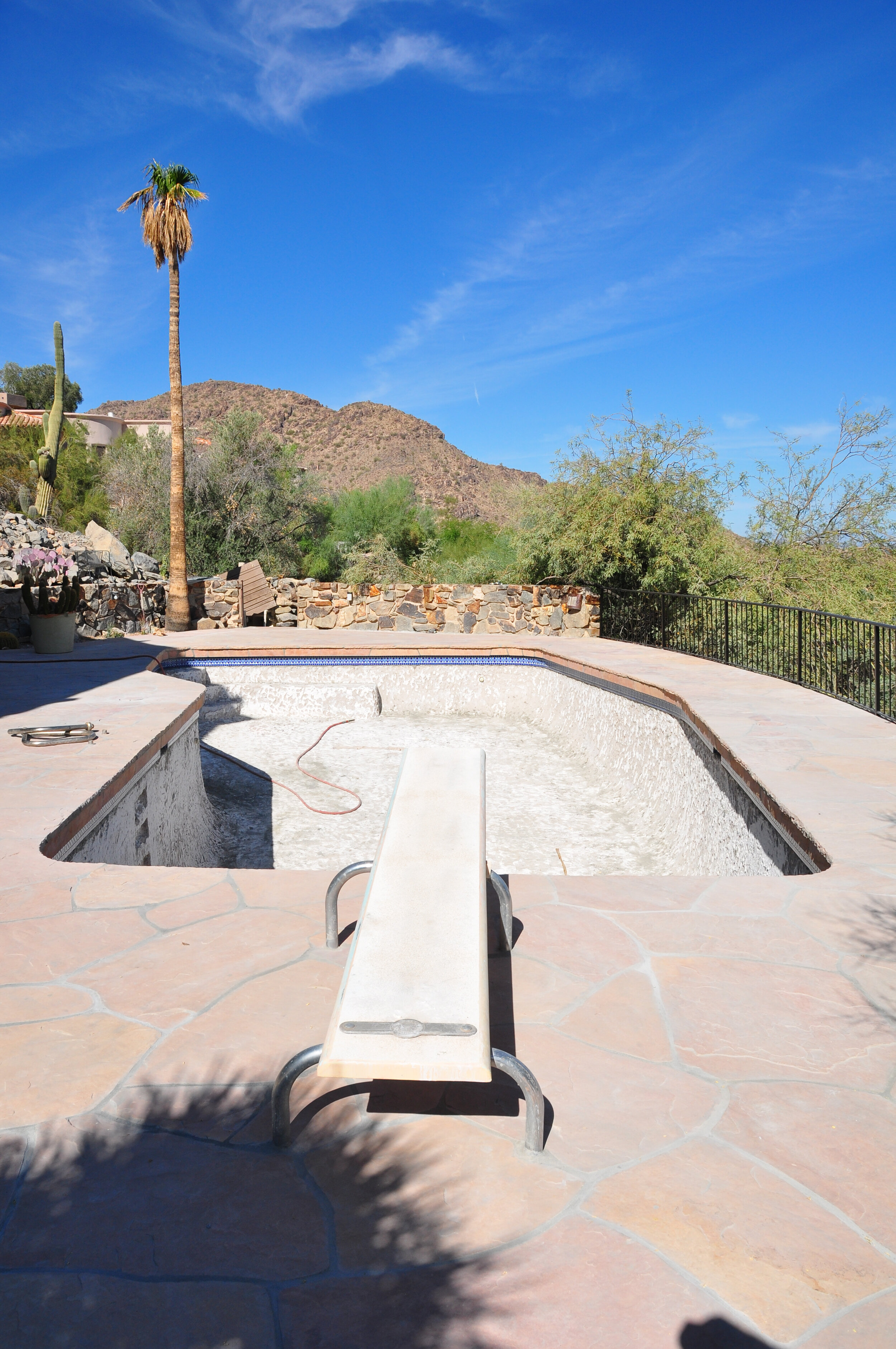 Empty in-ground swimming pool under a clear blue sky in a desert landscape with mountains and sparse vegetation.