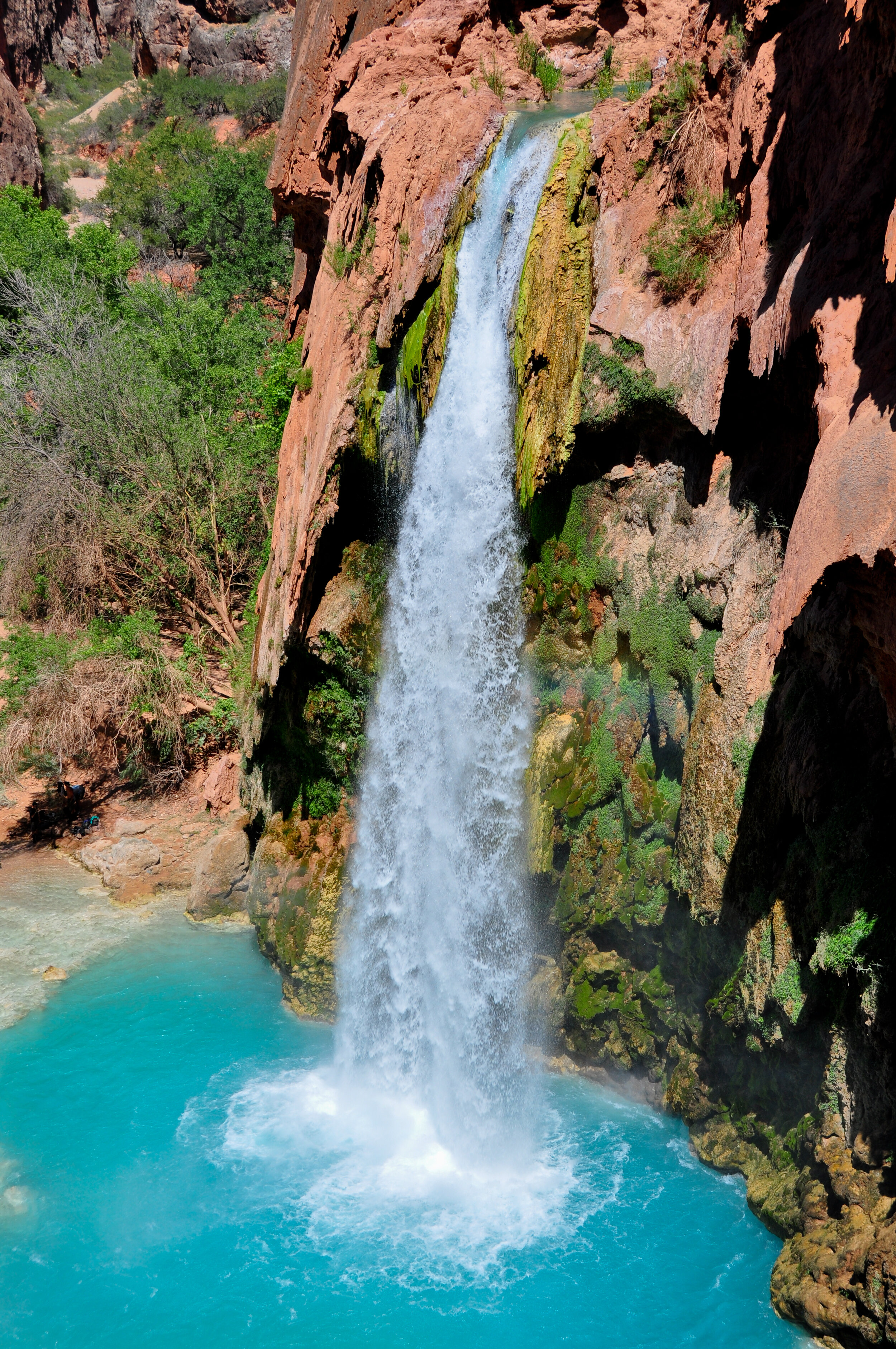 Waterfall cascading into a turquoise pool surrounded by rocky cliffs and greenery.
