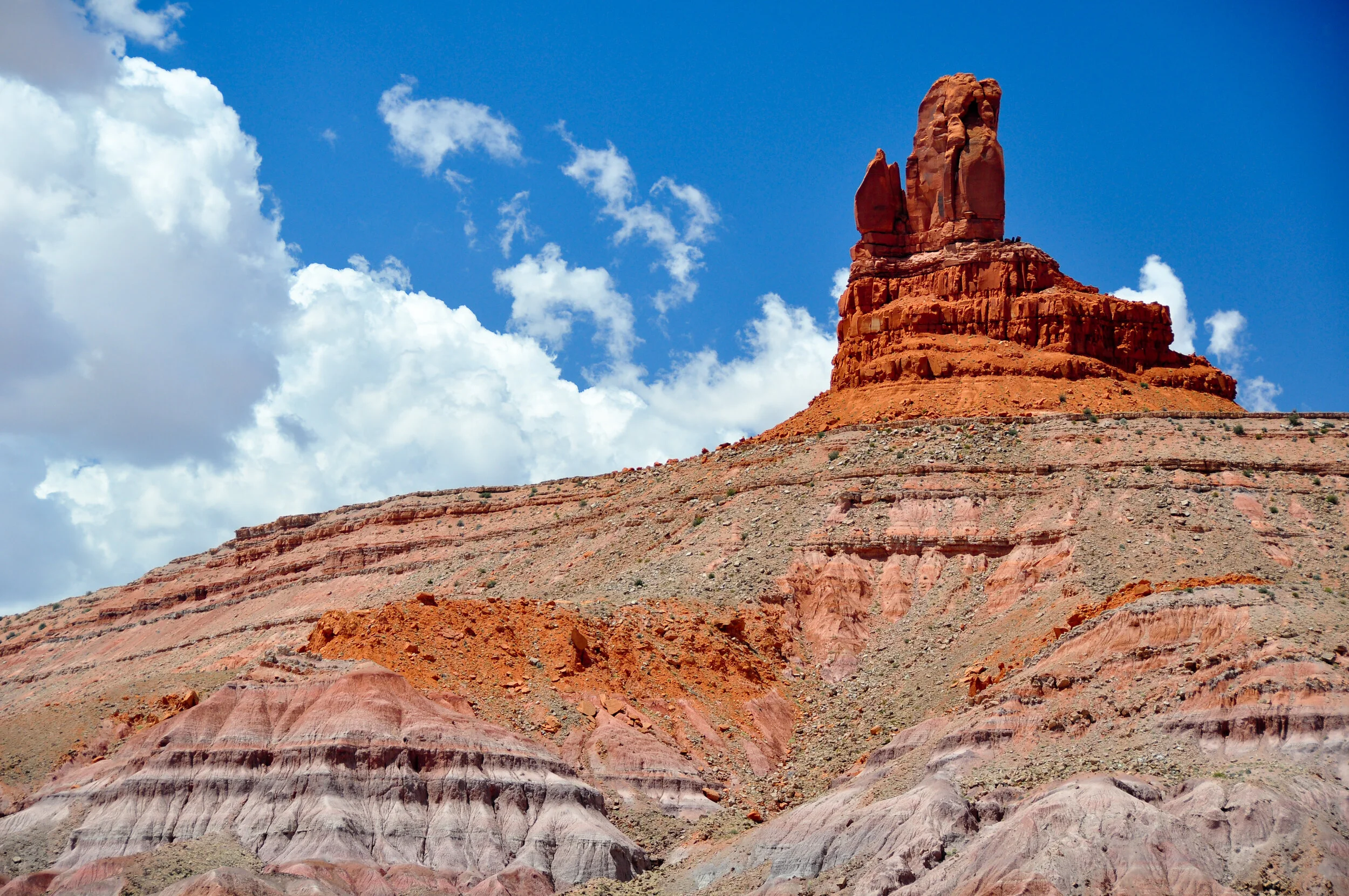 A red rock formation in a desert landscape with a blue sky and white clouds.