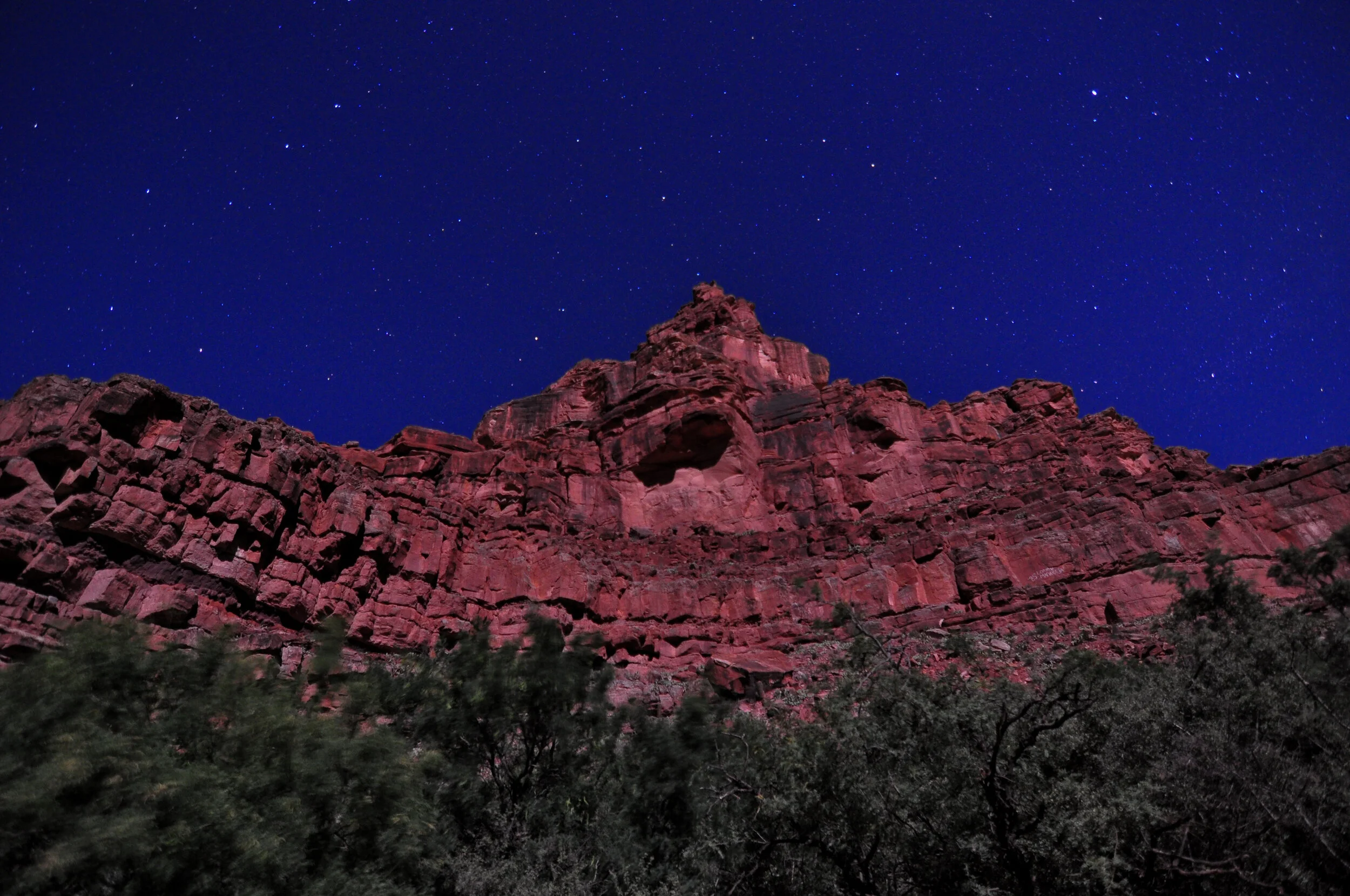Nighttime view of a red rocky mountain with a clear starry sky in the background.