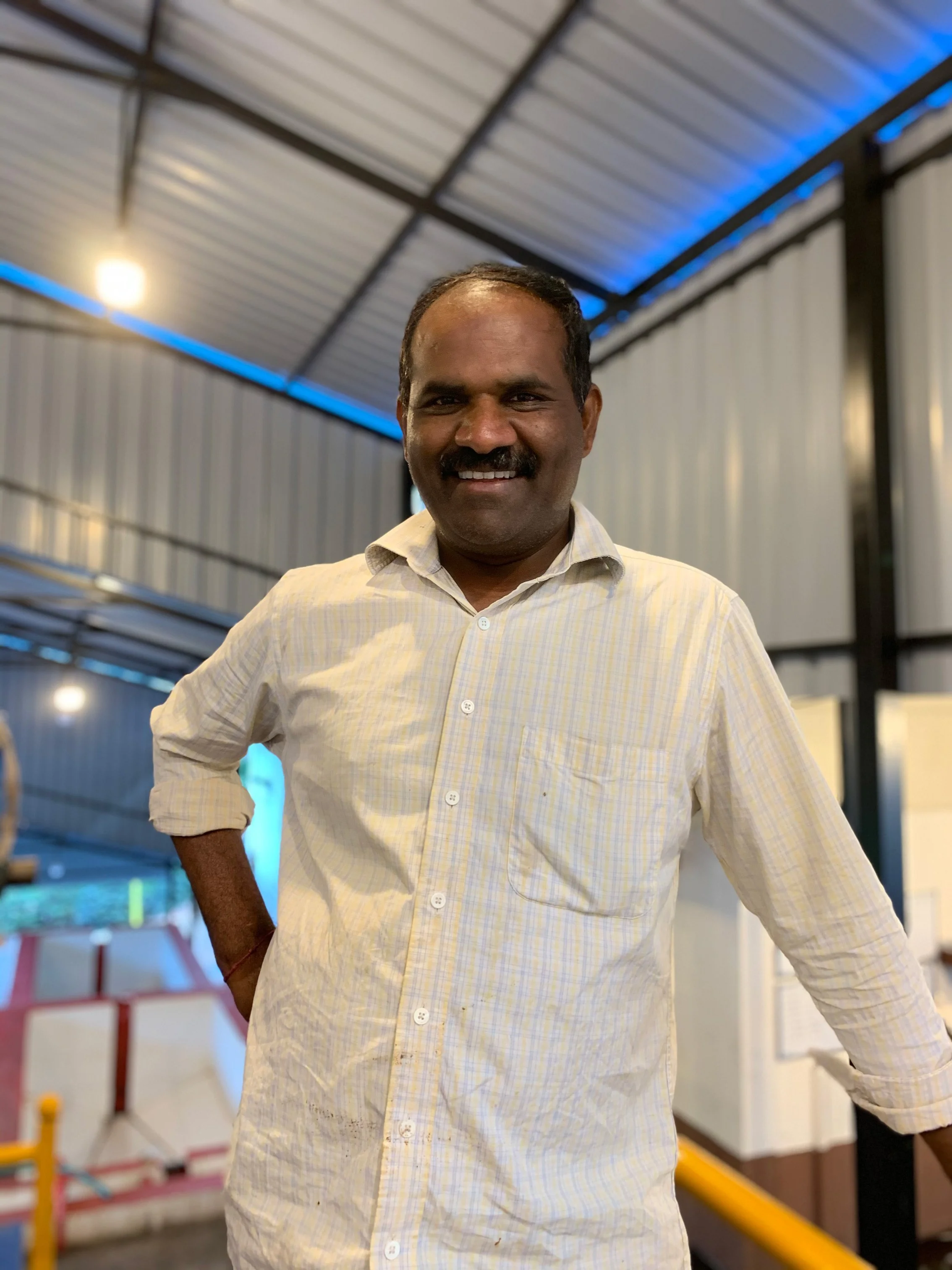 Man smiling and standing indoors with a warehouse or industrial setting in the background.