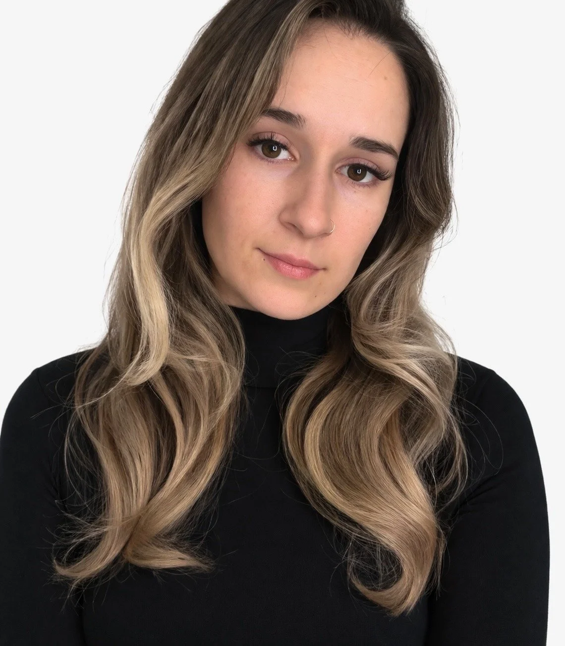 A young woman with long, wavy light brown hair wearing a black turtleneck, looking into the camera with a slight smile against a plain white background.