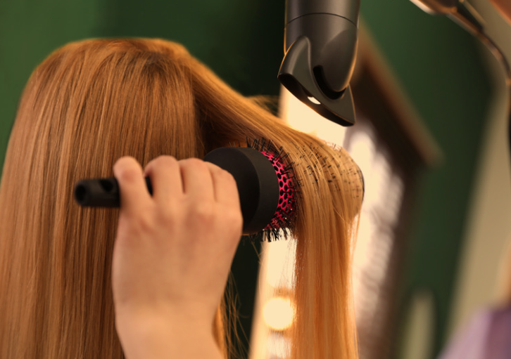 A person with straight, reddish hair is blow-drying their hair with a black and pink hair dryer.