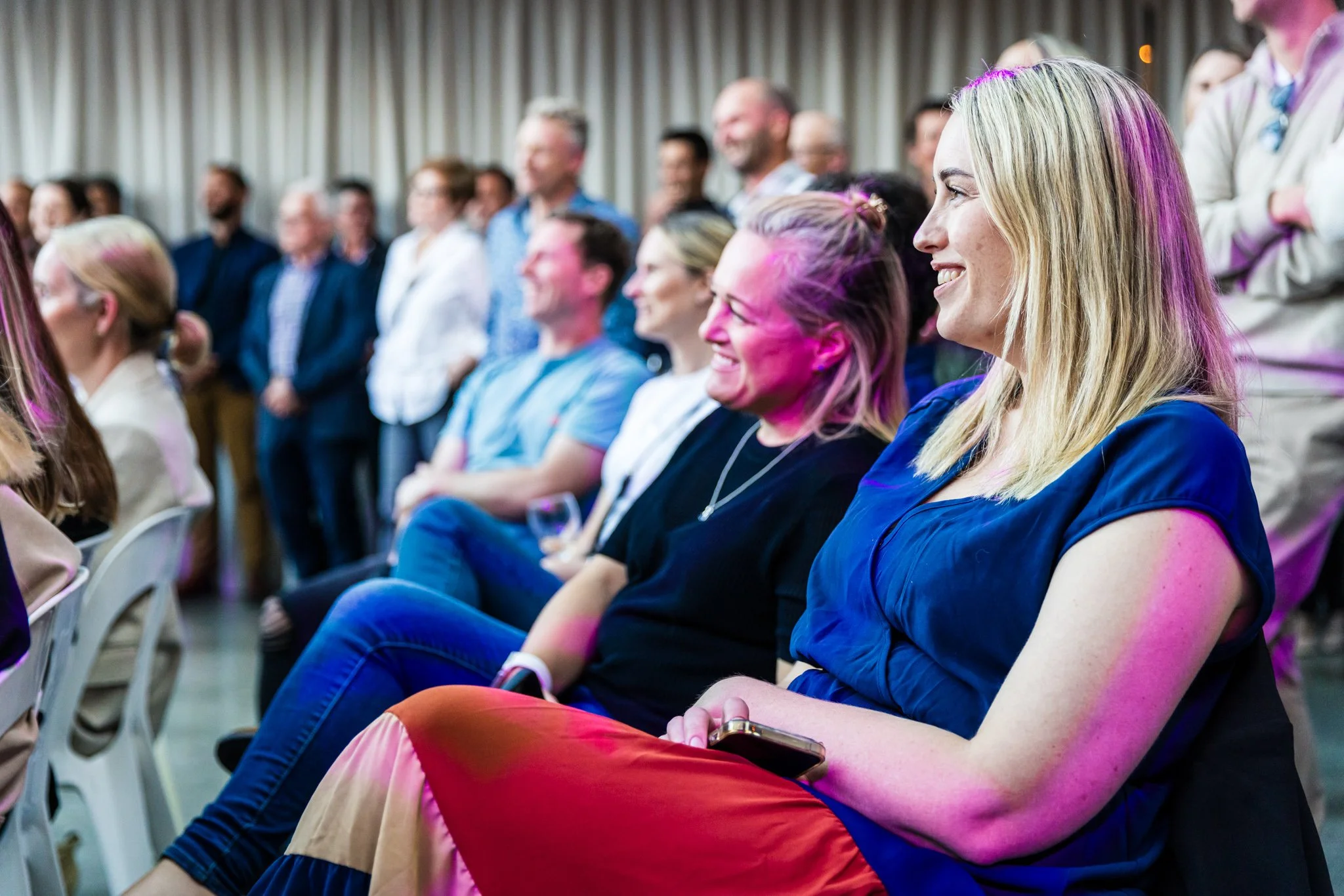 Group of smiling people sitting and standing at an indoor event.