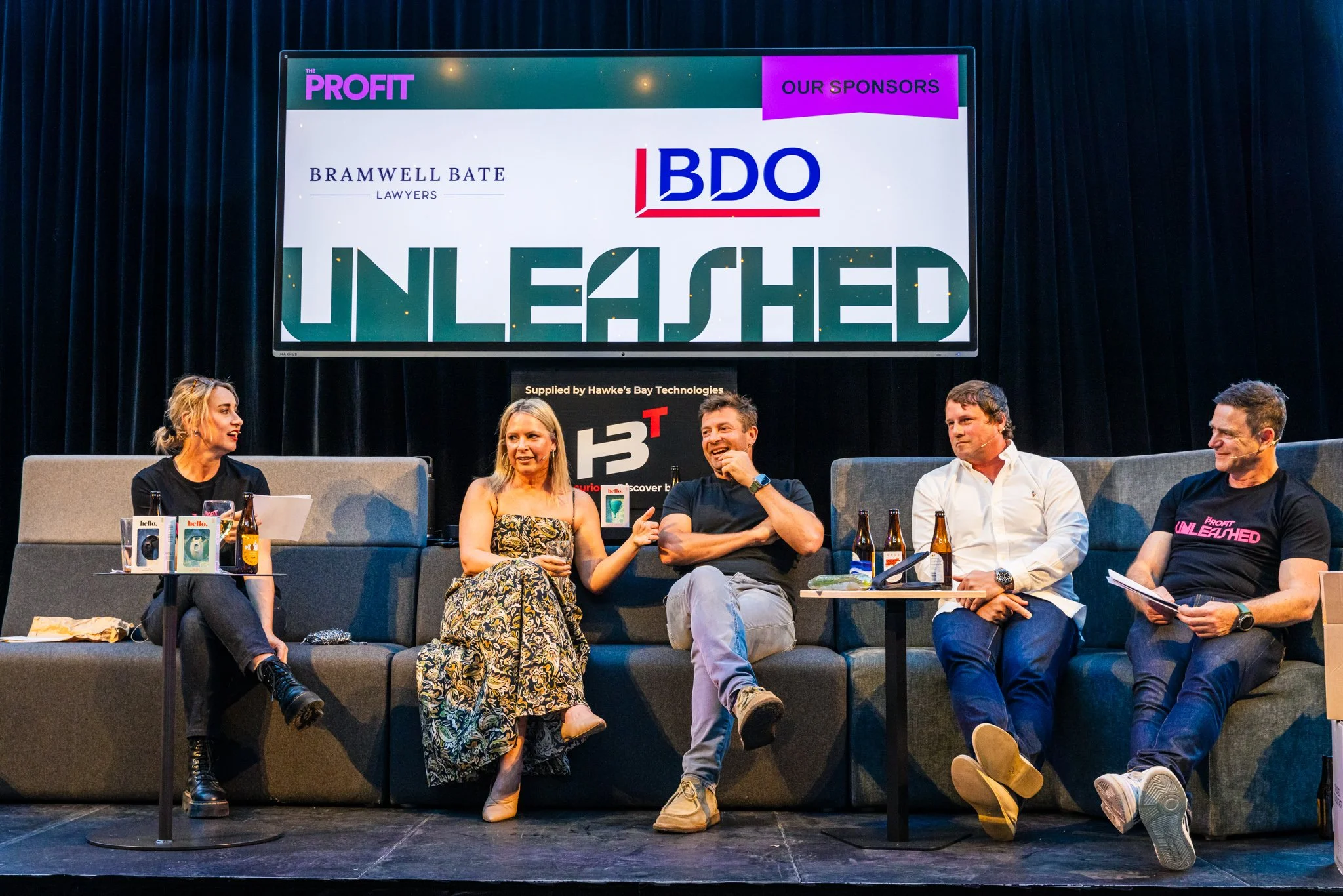 Five people sitting on a stage having a panel discussion, with a large monitor behind them displaying the words 'Profit Unleashed' and the logos of sponsors Bramwell Bate Lawyers and BDO.