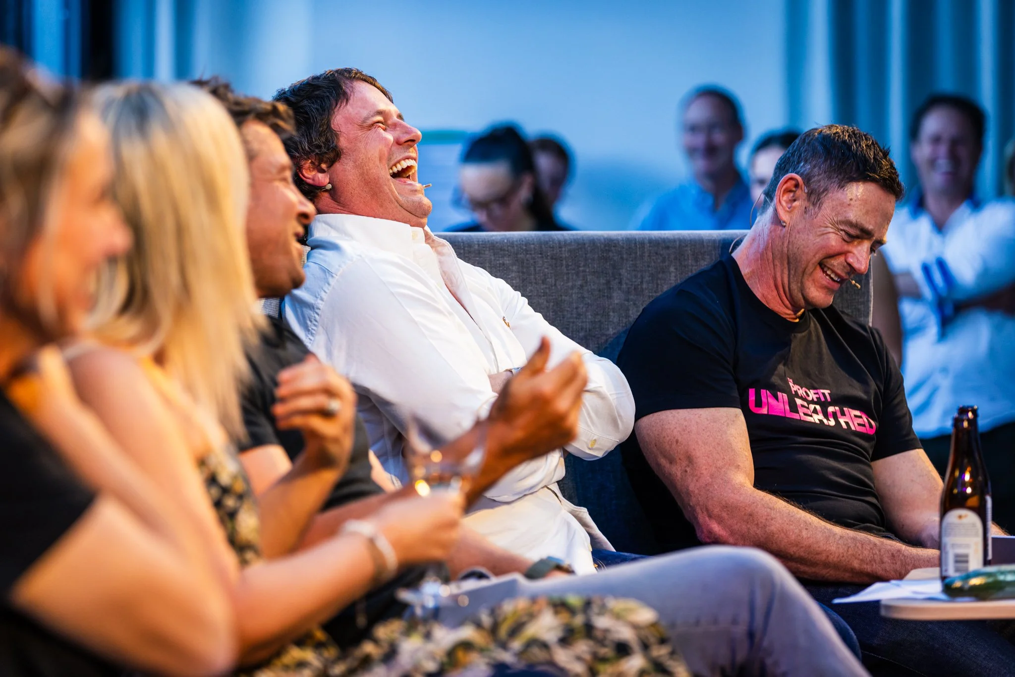 Group of people seated on a couch, laughing and enjoying a moment together in a social setting.