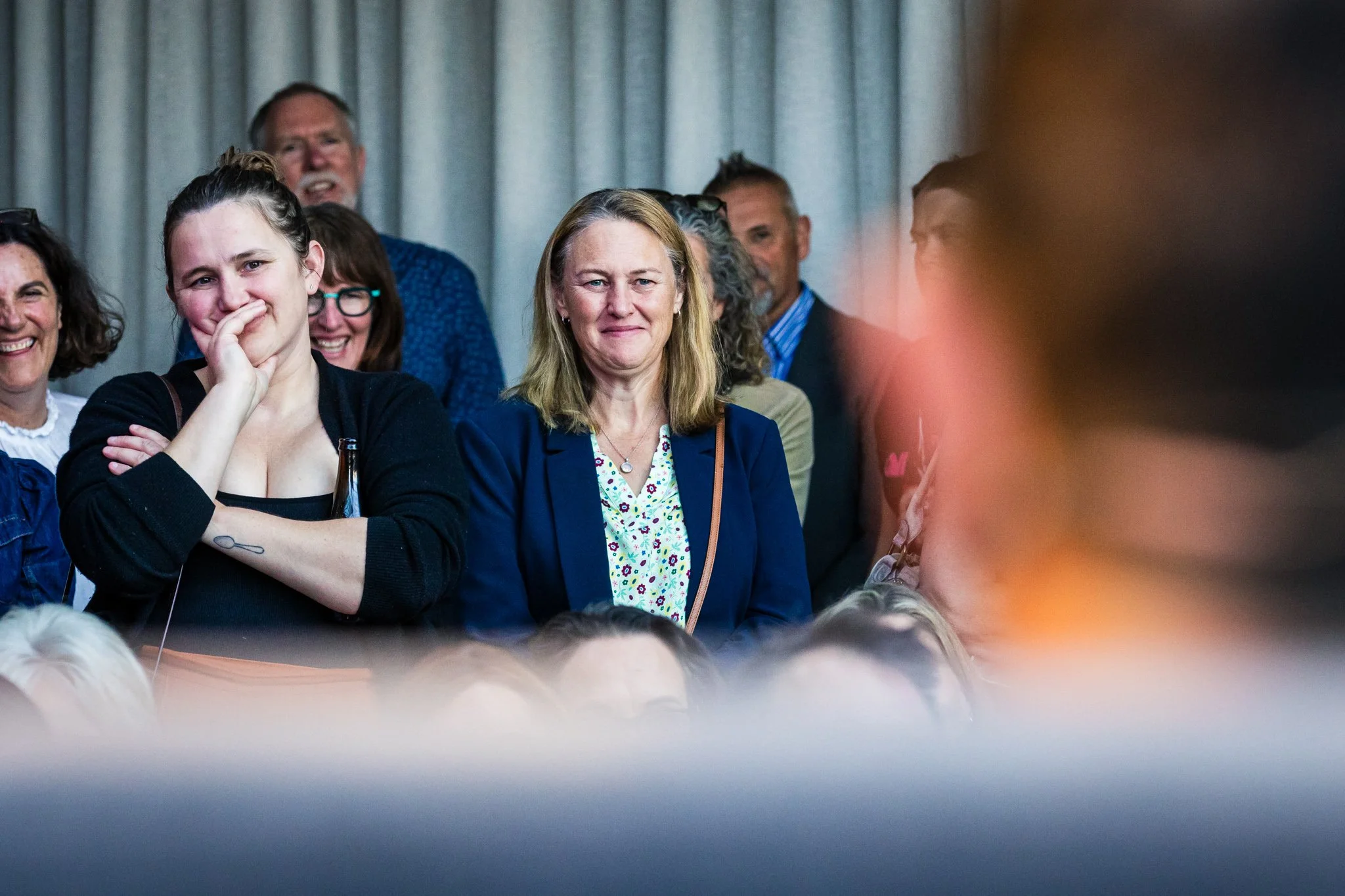 Group of people standing together at an indoor event, some smiling and others looking serious.