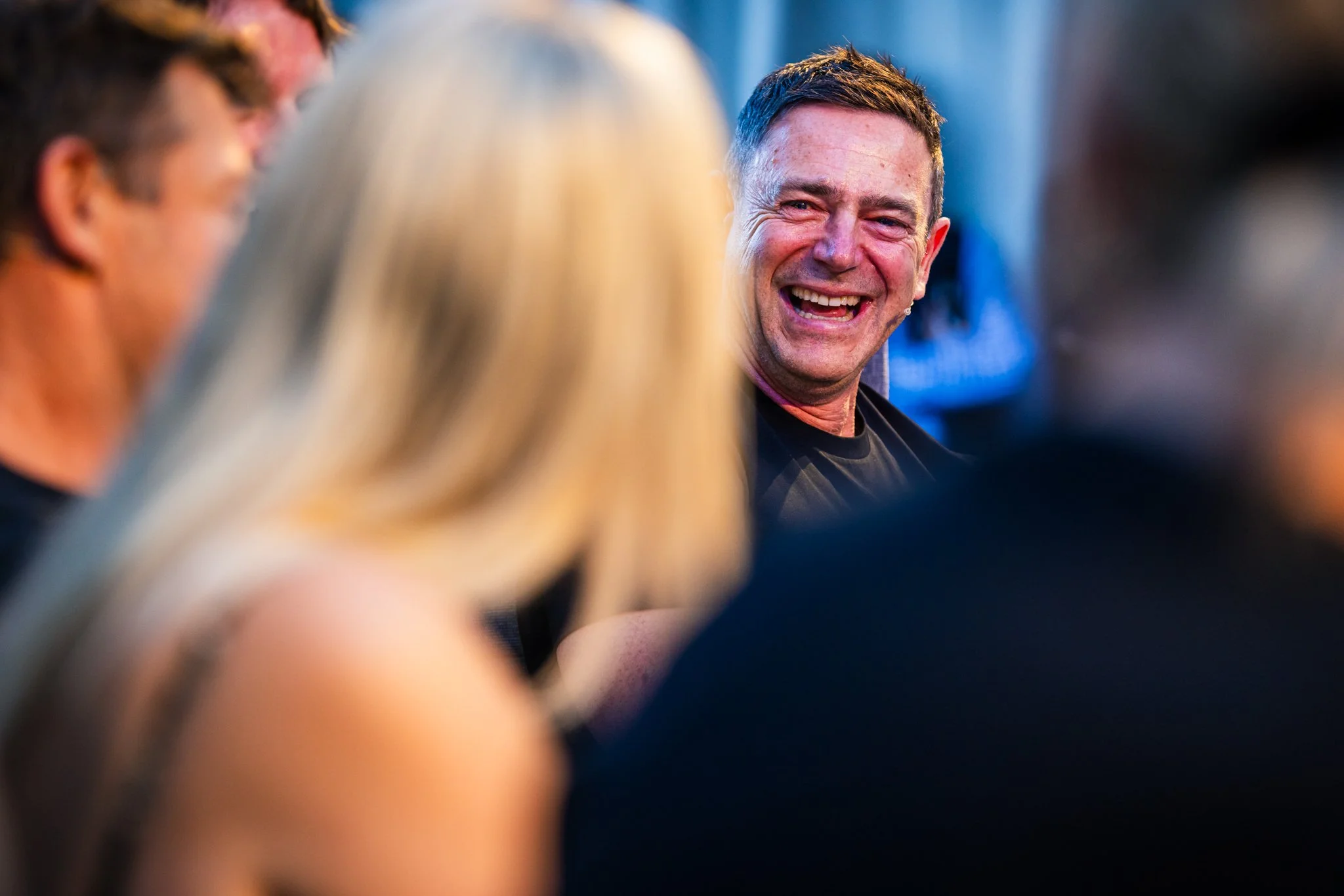 A man with short dark hair is smiling and laughing among a group of people at a social gathering.