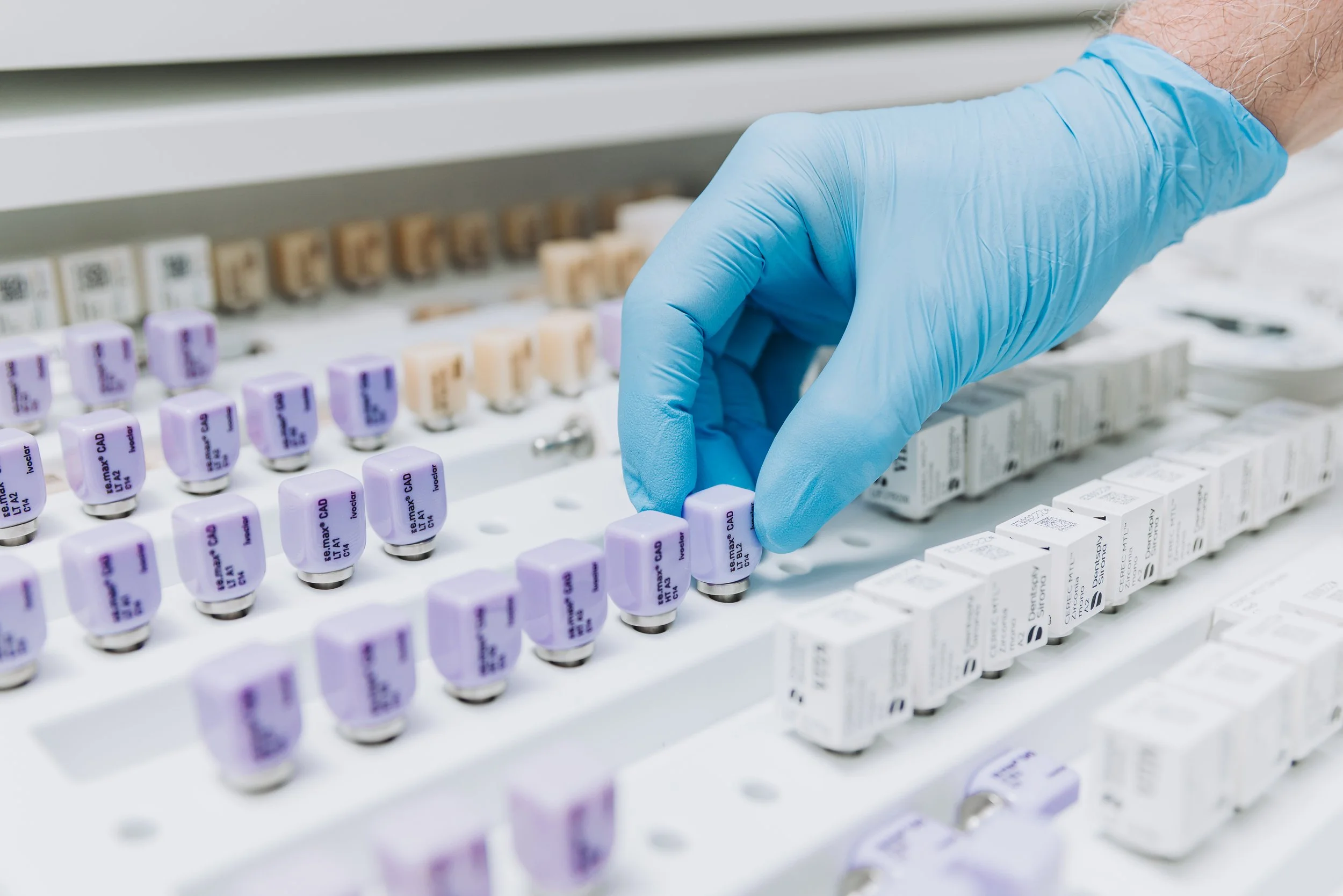 A gloved hand handling a vial among multiple vials and boxes of vaccines in a medical setting.