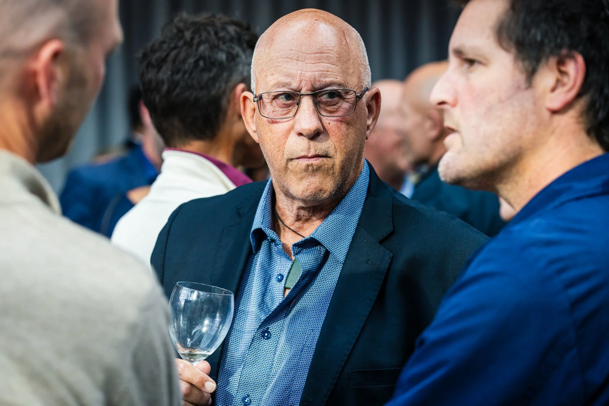 A group of people engaging in conversation at an event, with one man holding a glass.