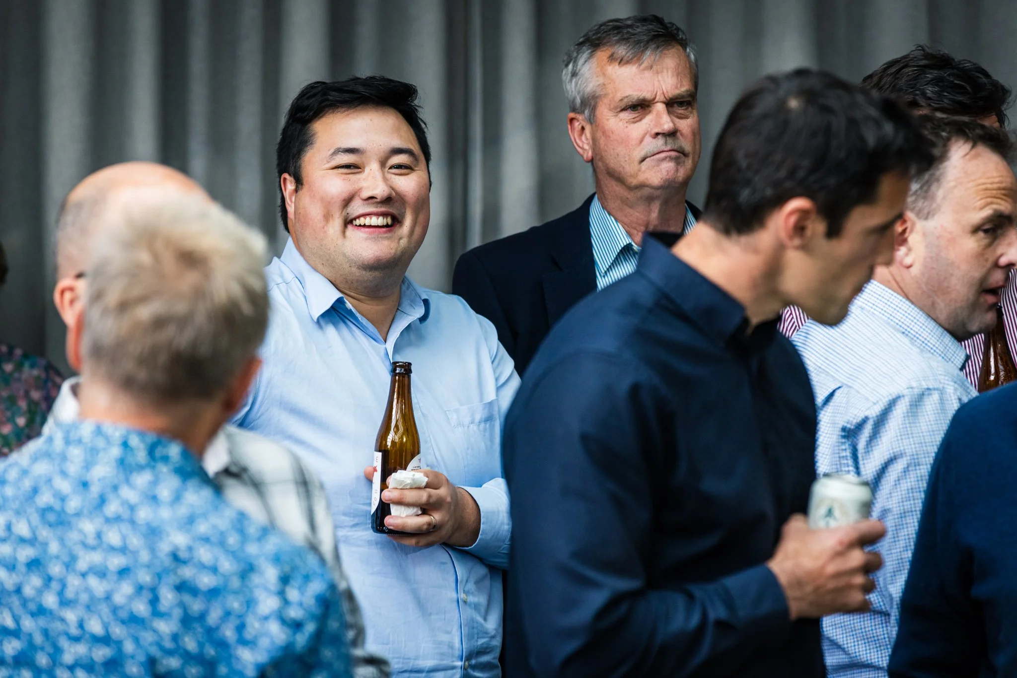 Group of men at a social gathering, some holding drinks, in a professional or casual setting.