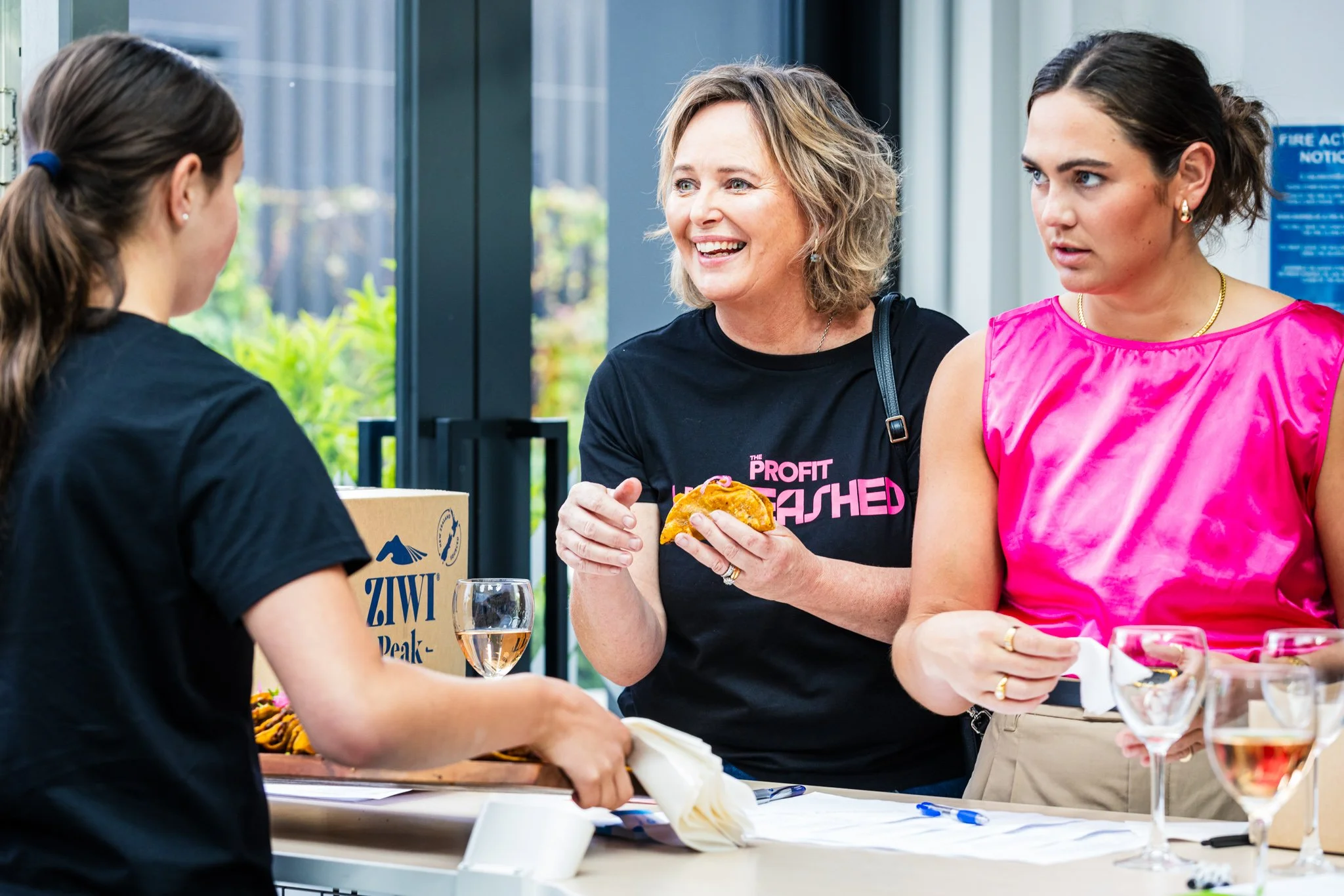 Three women are engaged in conversation at a table with wine glasses, snacks, and a ZWIT Peak box in the background.