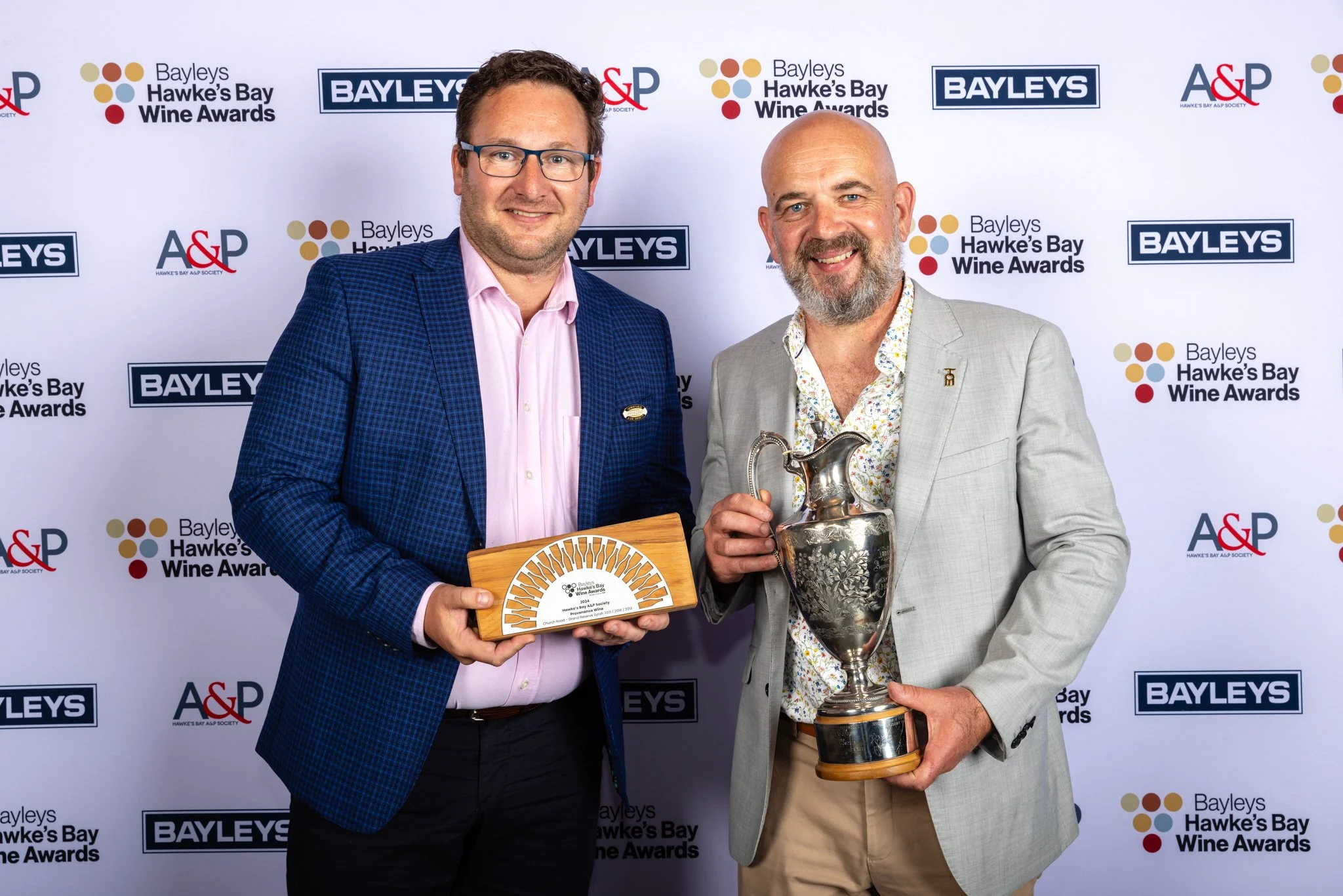 Two men in suits holding awards at the Bayleys Hawke's Bay Wine Awards, with a backdrop displaying logos of Bayleys, A&P, and the Hawke's Bay Wine Awards.
