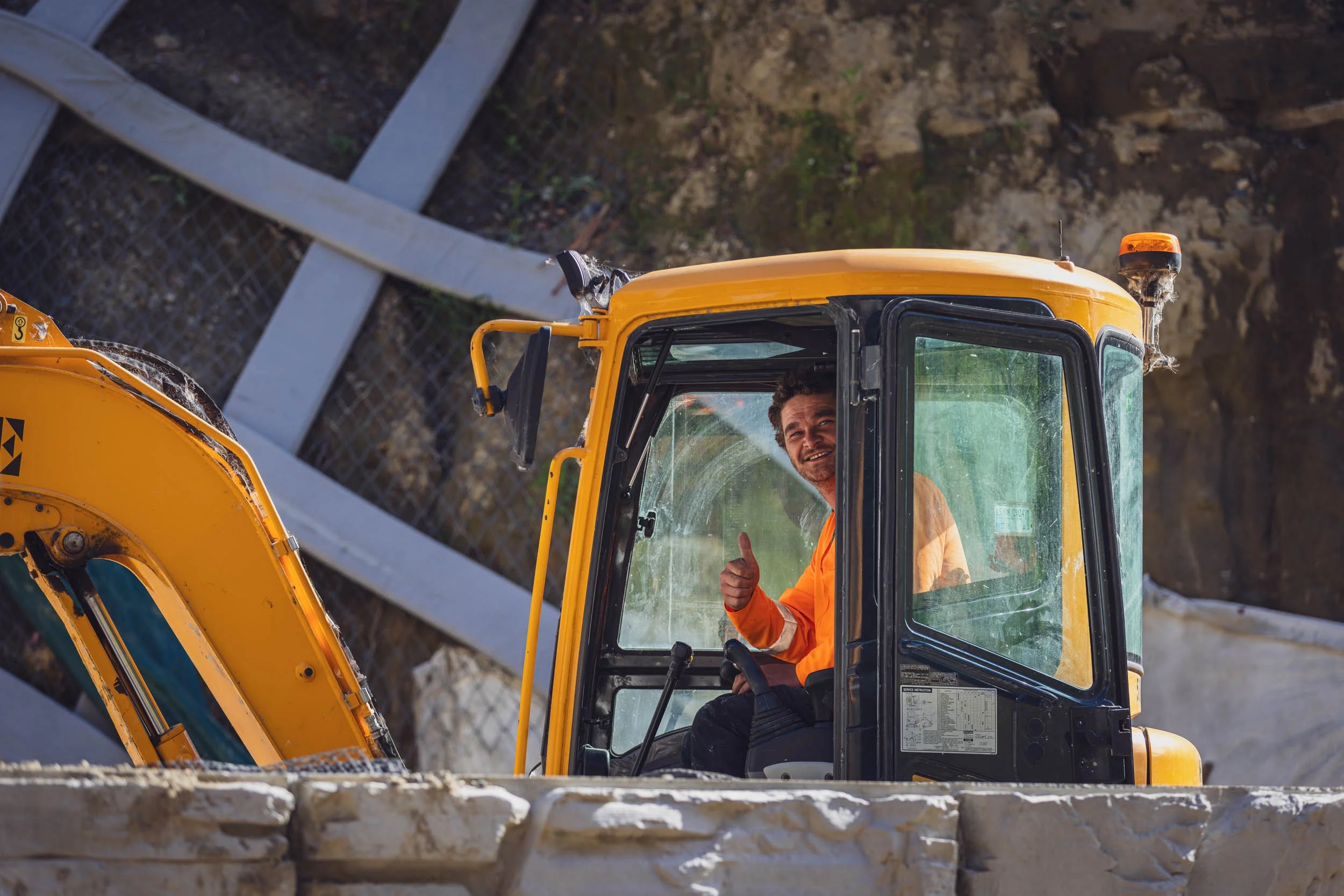 A construction worker giving the thumbs up whilst sat in a yellow excavator