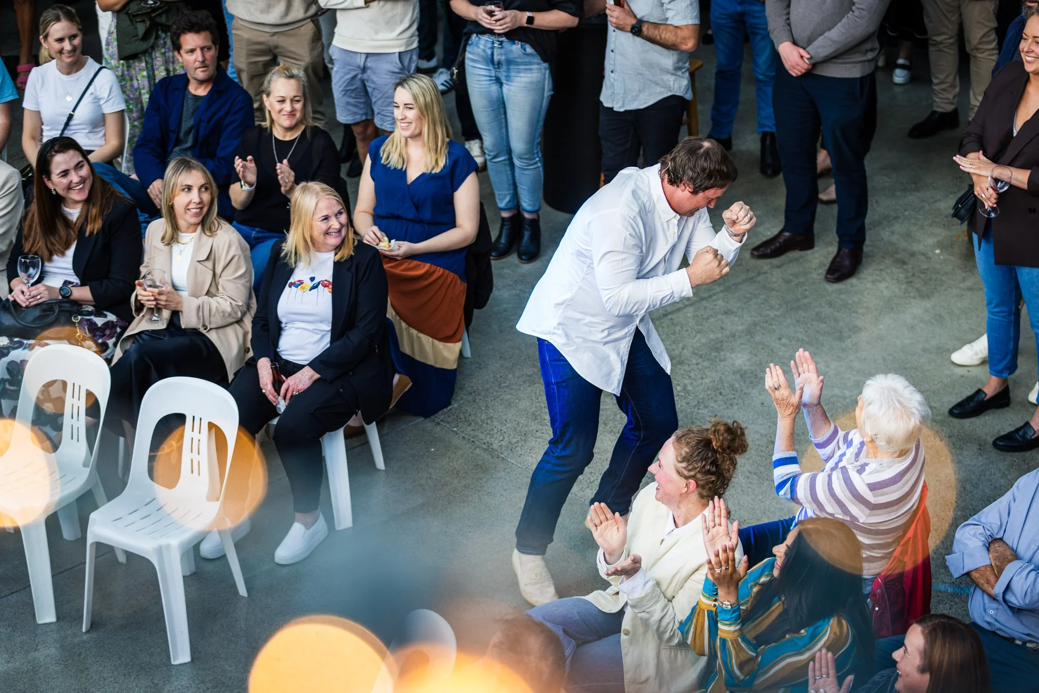 A group of people at an indoor event, with one man celebrating and five women clapping and smiling around him.