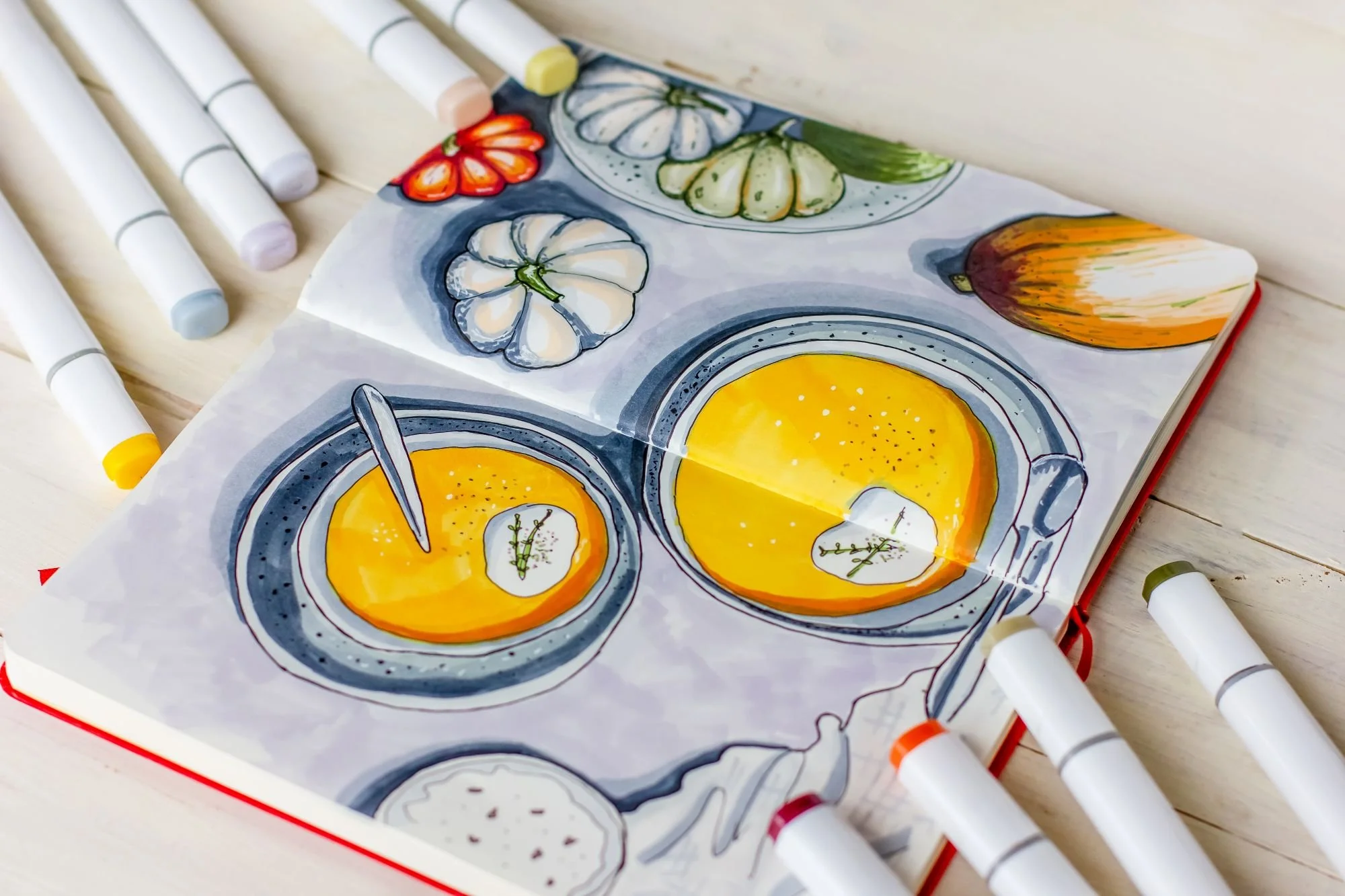 sketchbook with pumpkin soup drawings surrounded by alcohol markers