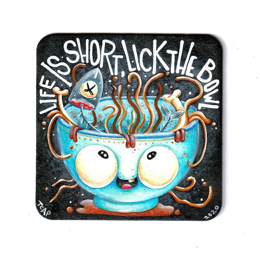 cardboard coaster on the white background featuring cartoon bowl with big eyes and words Life is short lick the bowl