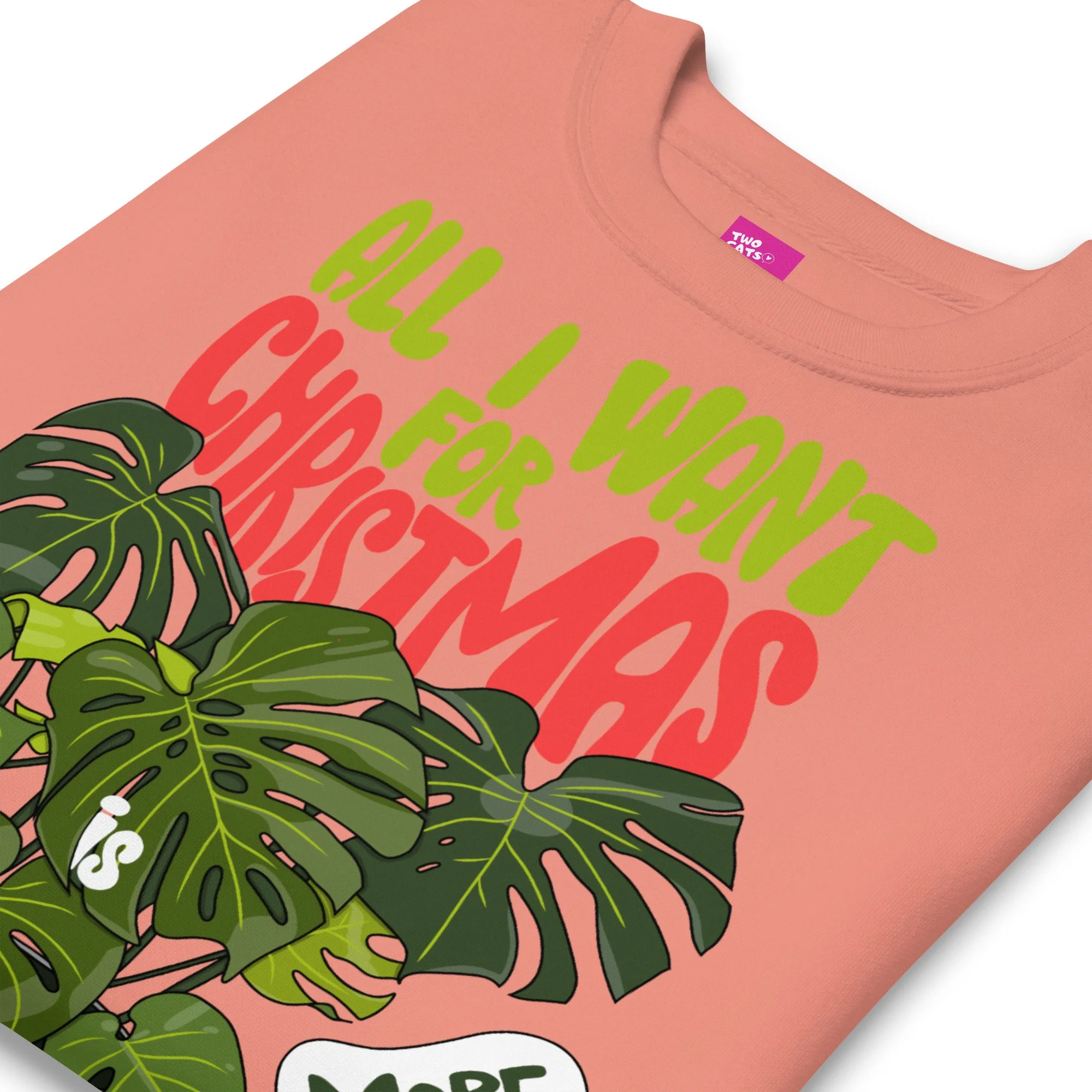 folded dusty rose cozy sweatshirt features a cute Monstera Deliciosa cartoon character in a pot, proclaiming, 'All I want for Christmas is more plants'