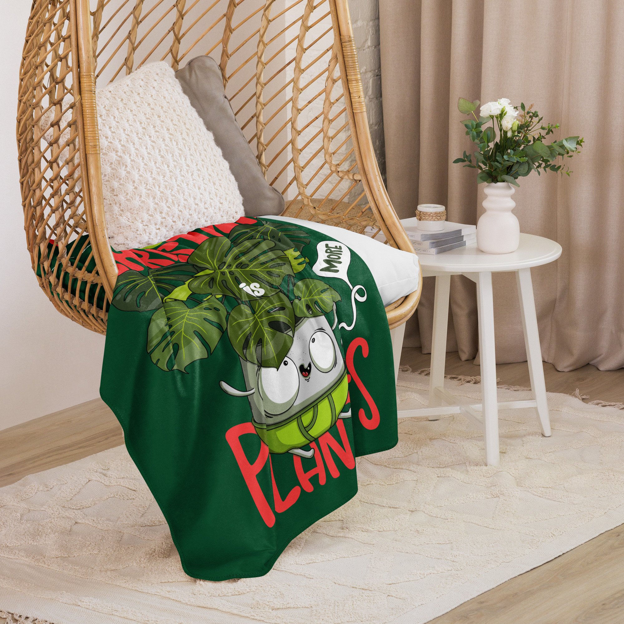a chair with a cozy and soft sherpa blanket featuring a cute cartoon Swiss Cheese plant in a pot with the humorous statement, "All I want for Christmas is more plants" laid on it