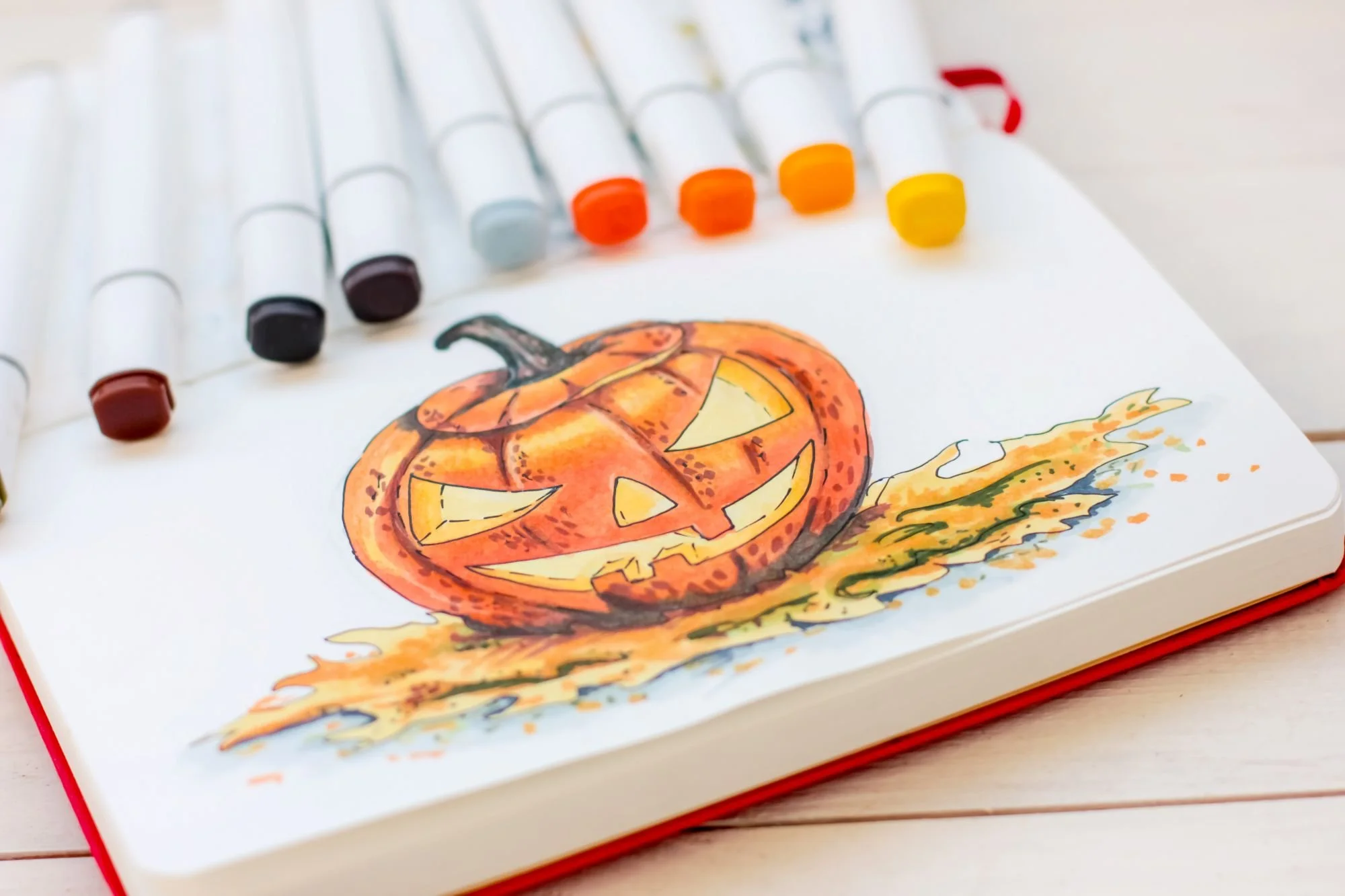cartoon Halloween pumpkin drawings in a sketchbook surrounded by alcohol markers