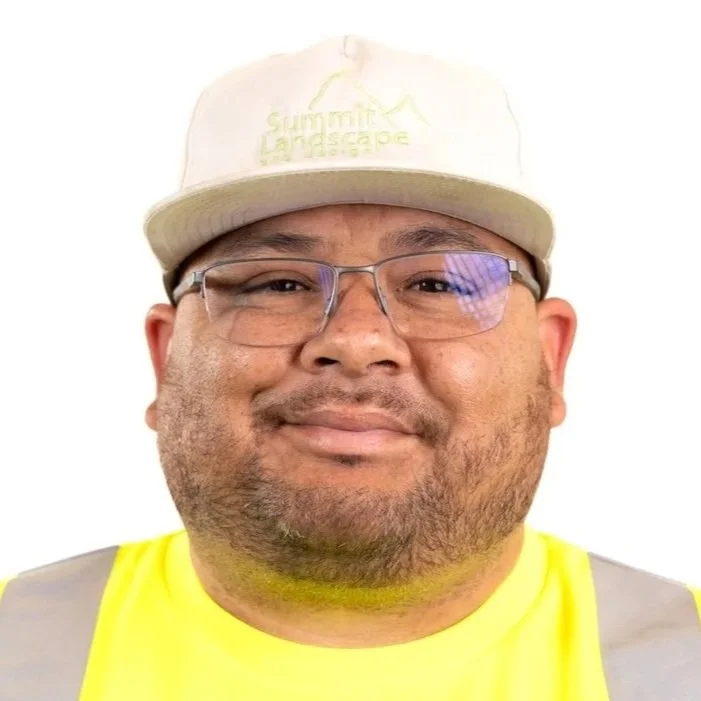 A man wearing a beige baseball cap with the words 'Summit Landscape' embroidered on it, glasses, and a bright yellow safety vest.