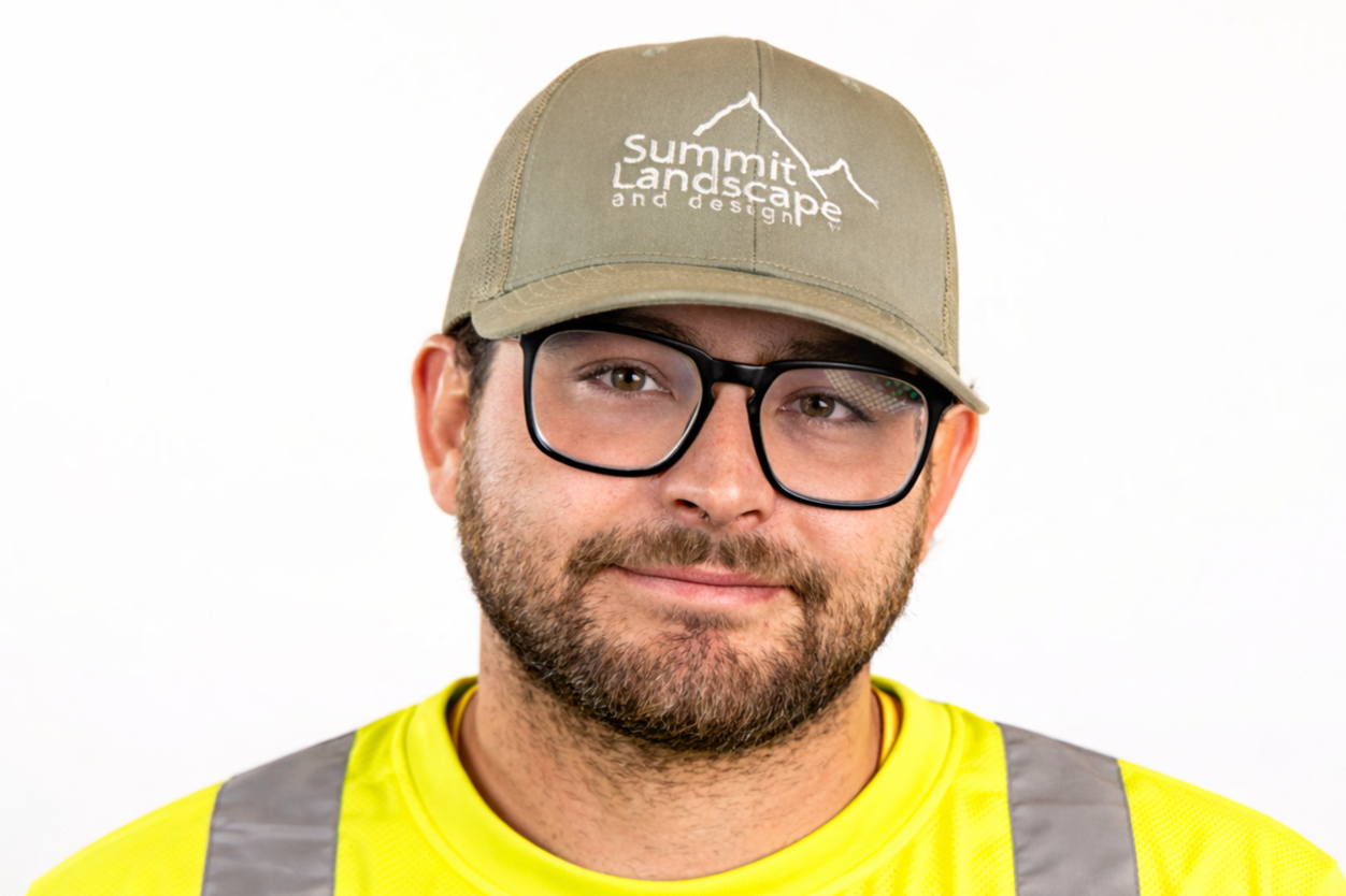 A man wearing a beige cap that says 'Summit Landscape and Design,' black glasses, and a yellow safety vest, smiling against a white background.