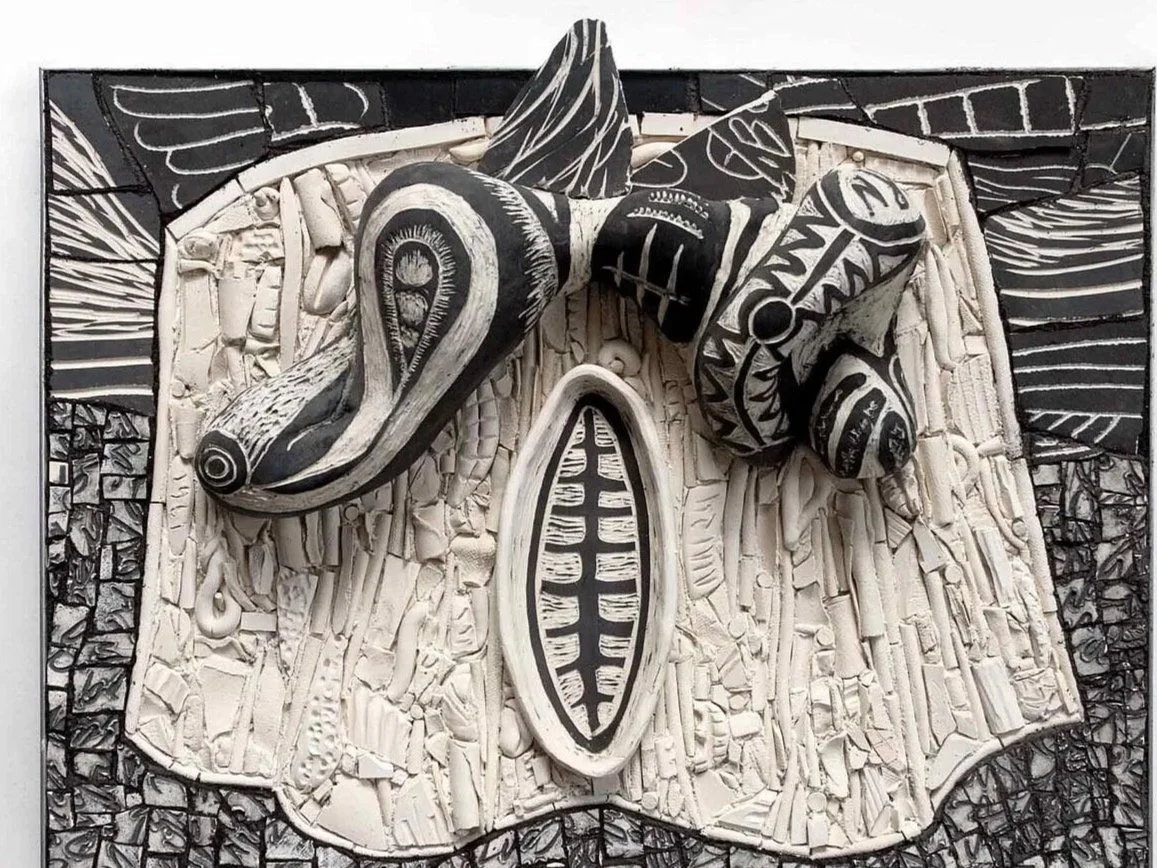 A black-and-white carved figure depicting an apparition with wings floating above a shroud, surrounded by  patterns and shapes containing broken text and poems.