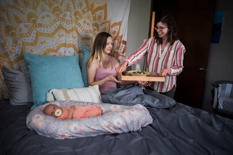 Postpartum doula serving nourishing warm meal to a resting mother during in-home postpartum care visit in Lincoln Nebraska