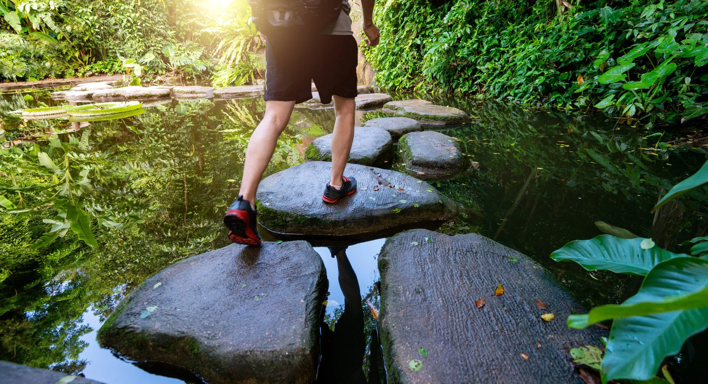 Single person stepping across river stones, metaphor for individual coaching journey