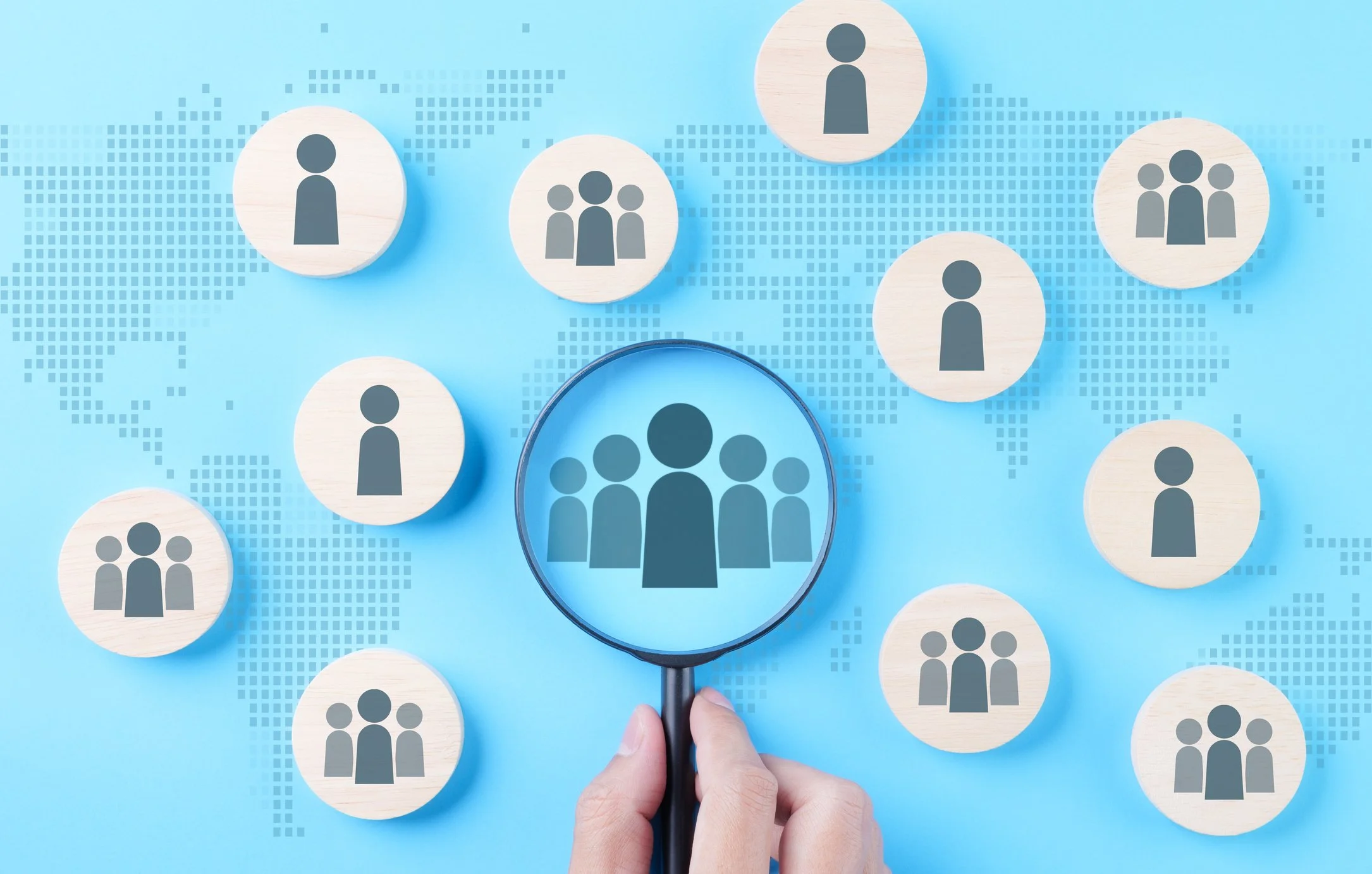A hand holding a magnifying glass over icons of people, highlighting a group of three, representing assessing a leadership team.