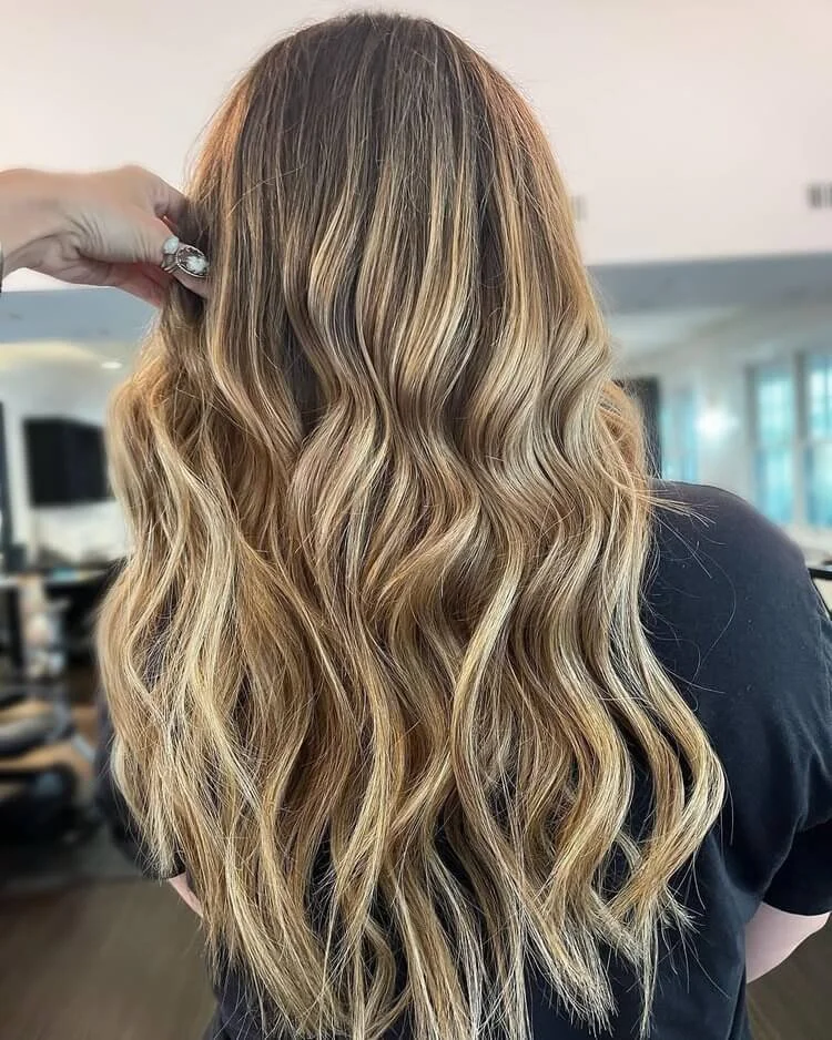 Long, wavy brunette hair with dimensional blonde highlights styled at TEAL Hair & Makeup Studio.
