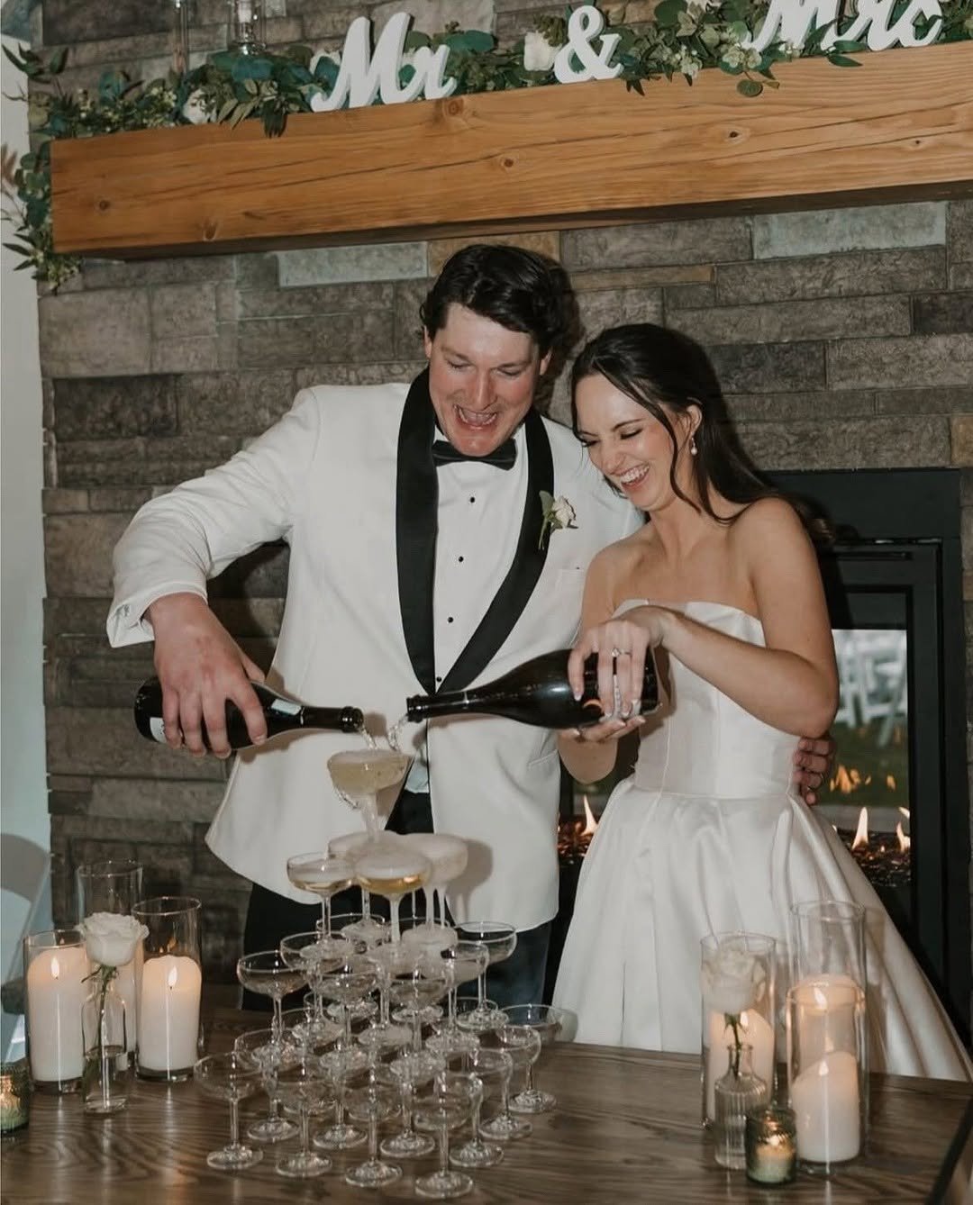 A joyful bride and groom pour champagne into a tower of glasses, with hair and makeup by TEAL Hair and Makeup Studio.