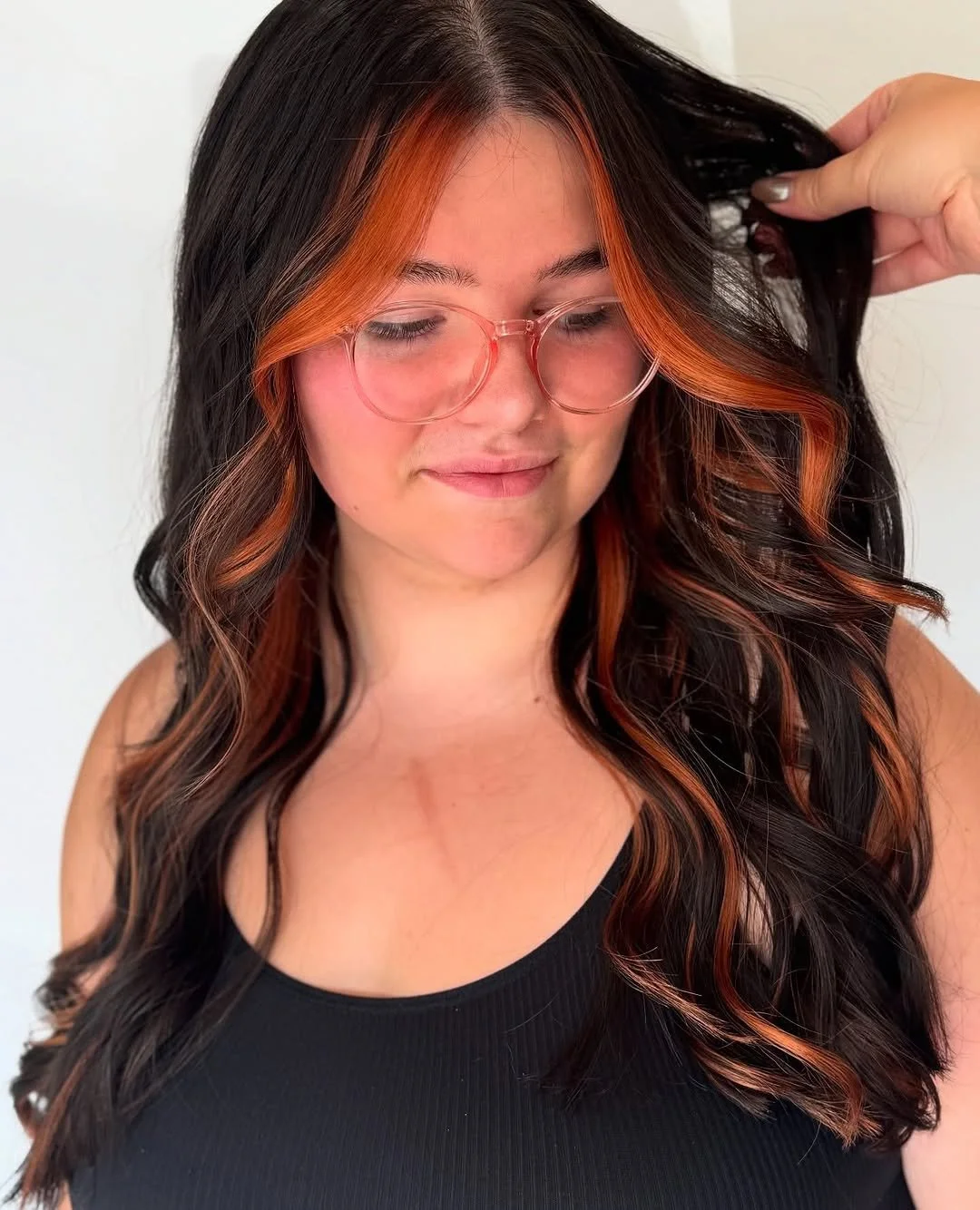  Woman with long dark hair and bold copper face-framing highlights styled in soft waves, showcasing a dimensional color transformation by TEAL Hair &amp; Makeup Studio. 