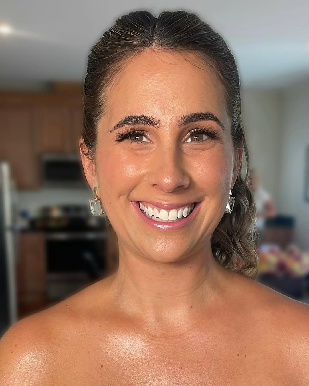  Smiling woman with glowing natural makeup and sleek pulled-back hairstyle, showcasing a polished beauty look by TEAL Hair &amp; Makeup Studio. 